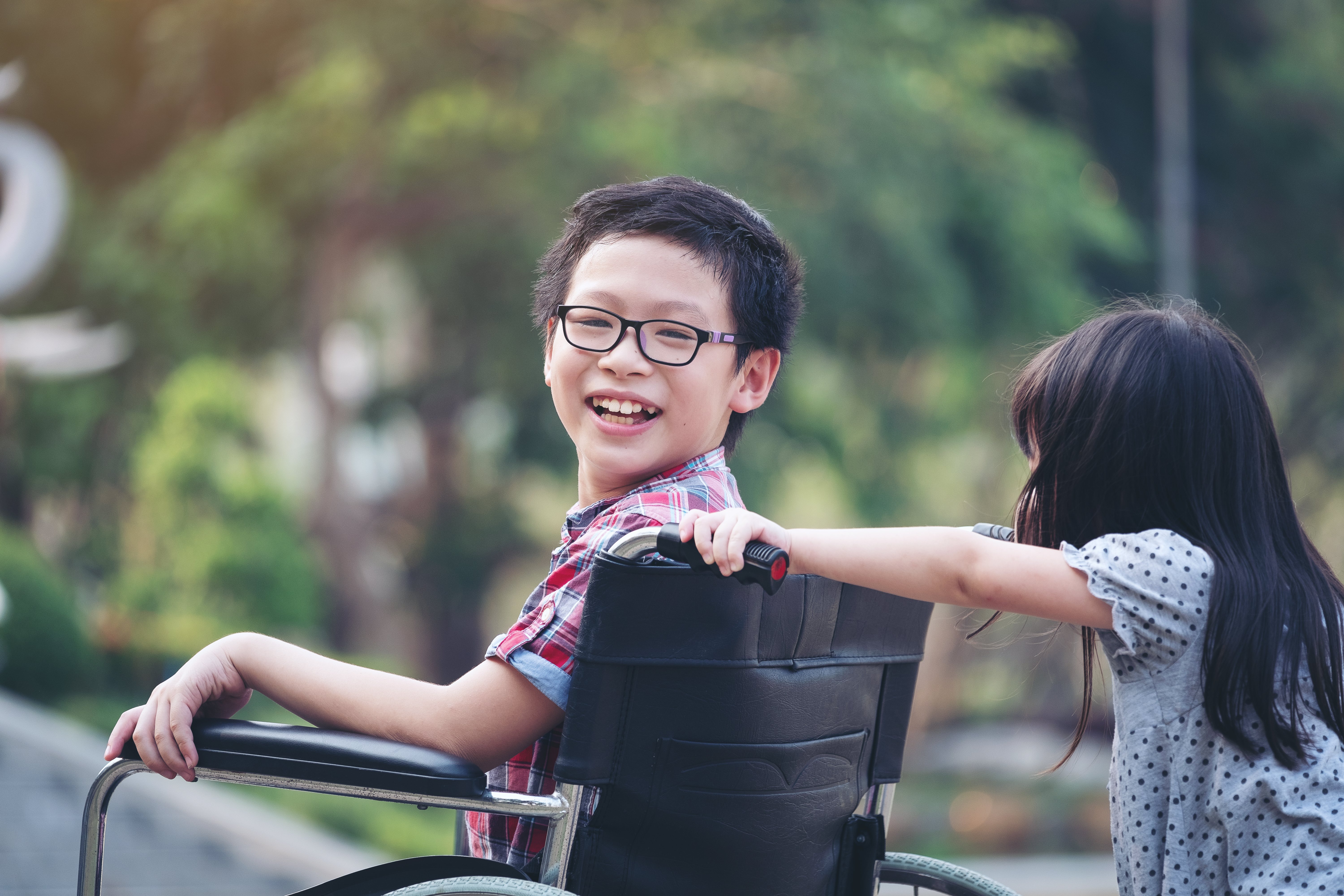 Portrait Of Happy Boy Sitting On Wheelchair With Sister|Photo: Getty Images