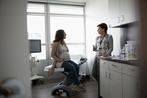 Female obstetrician talking with a pregnant patient in clinic examination room | Photo: Getty Images