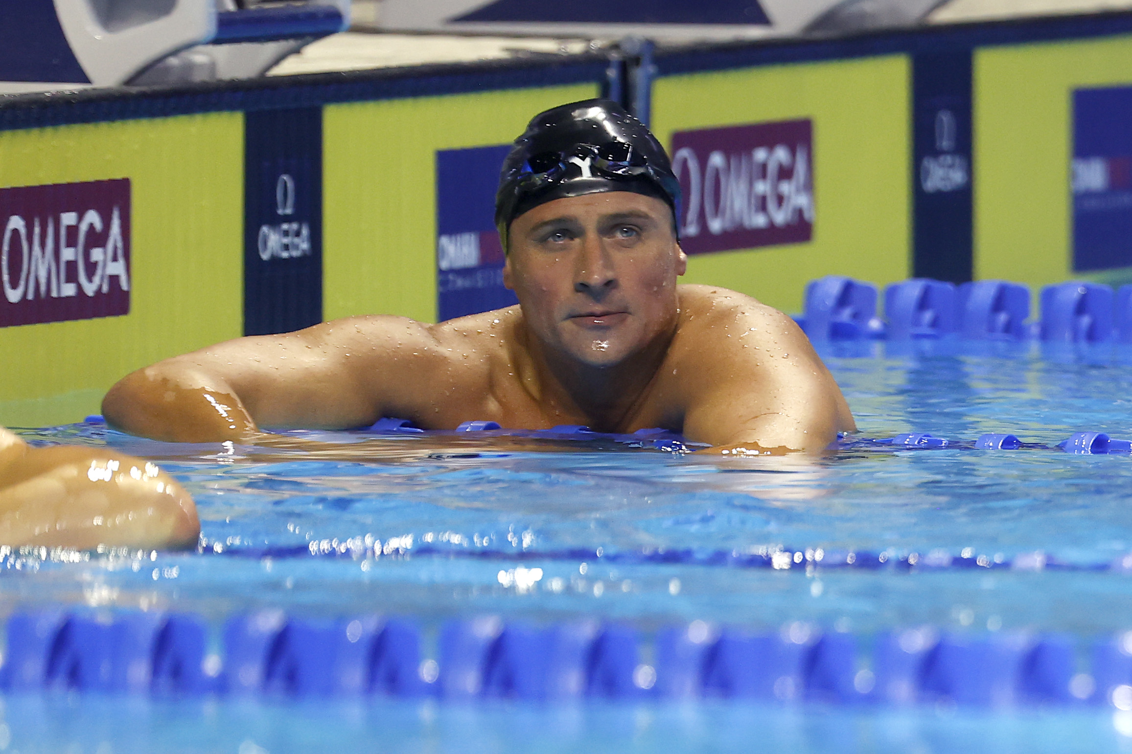 Ryan Lochte rests at the edge of the pool after competing in the men’s 200m individual medley final during the U.S. Olympic Team Trials. Wearing a black swim cap and goggles, the swimmer looks ahead while catching his breath in the water.