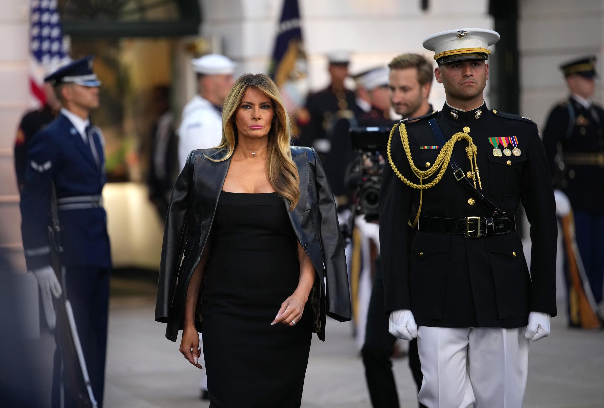 Walking toward the event, Melania Trump wears her hair in loose waves. Her defined jawline, contoured cheeks, and polished makeup create a striking, camera-ready look.