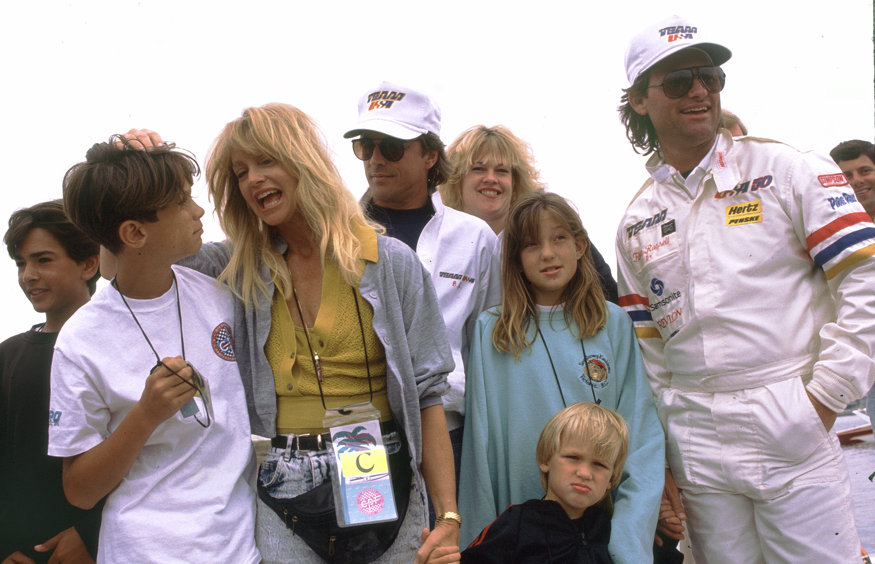 Goldie Hawn, Kurt Russell, and their children gather with Don Johnson and Melanie Griffith at a boat racing event in Long Beach. Casual and animated, Hawn playfully tousles her son's hair, while young Kate Hudson stands front and center.
