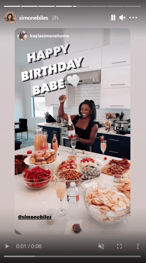 A screenshot from a video of Simone Biles posing in front of a table with several delicacies | Source: Instagram/simonebiles