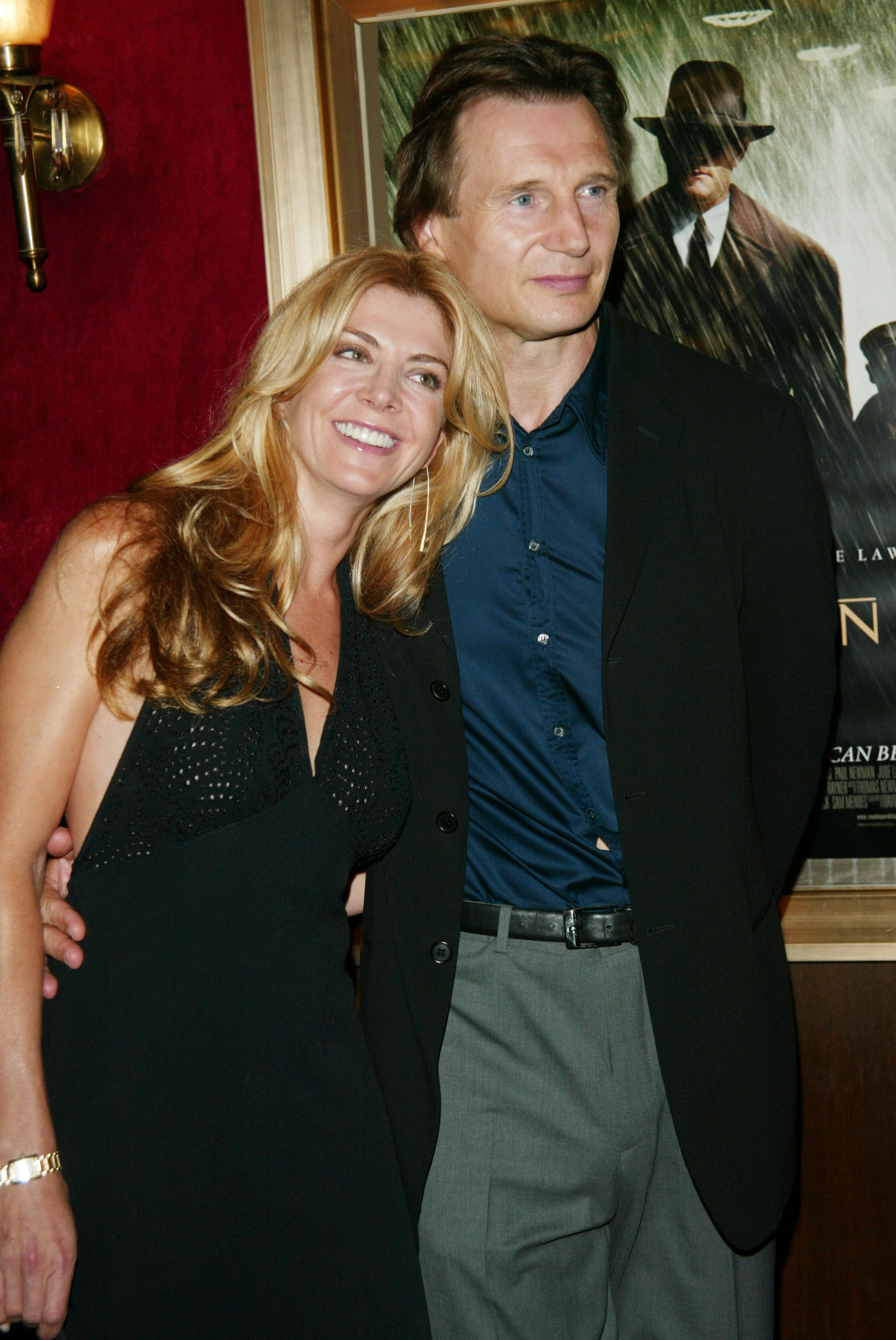 Natasha Richardson leans into Liam Neeson as they pose together at the Road to Perdition premiere at the Ziegfeld Theatre in New York City on July 9, 2002. Both smile for photographers while standing in front of the film’s promotional backdrop.