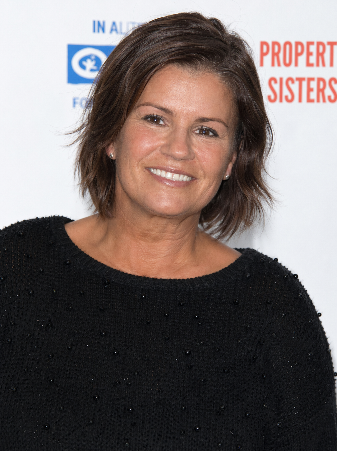 Kerry Katona smiles warmly at a Property Sisters event, wearing a black textured top and a natural, relaxed expression. | Source: ChatGPT