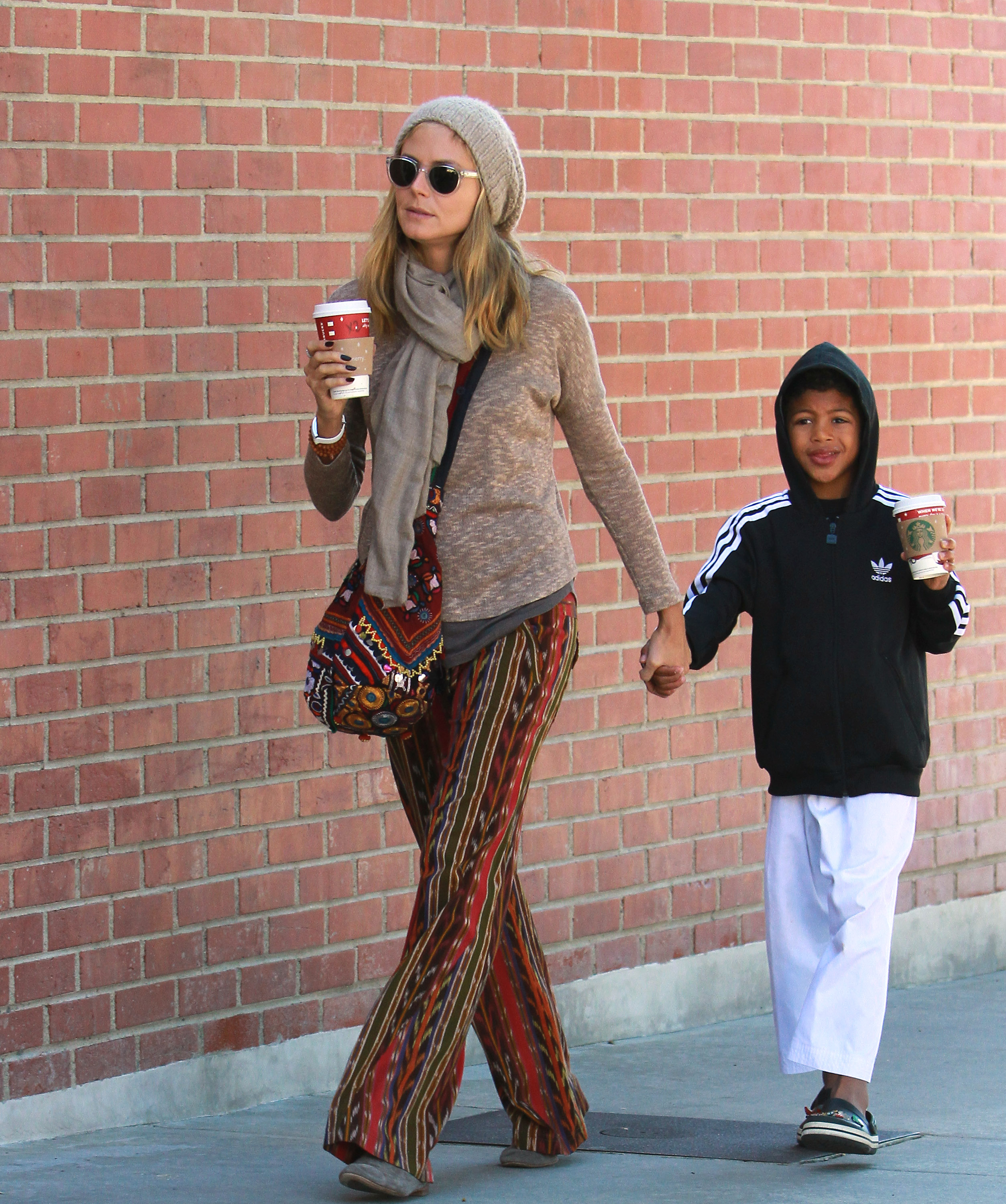 Walking in sync along a sunlit sidewalk in Brentwood, Heidi Klum keeps it effortlessly chic with coffee in hand, while Henry Samuel, relaxed in a hoodie and sneakers, mirrors her calm stride.