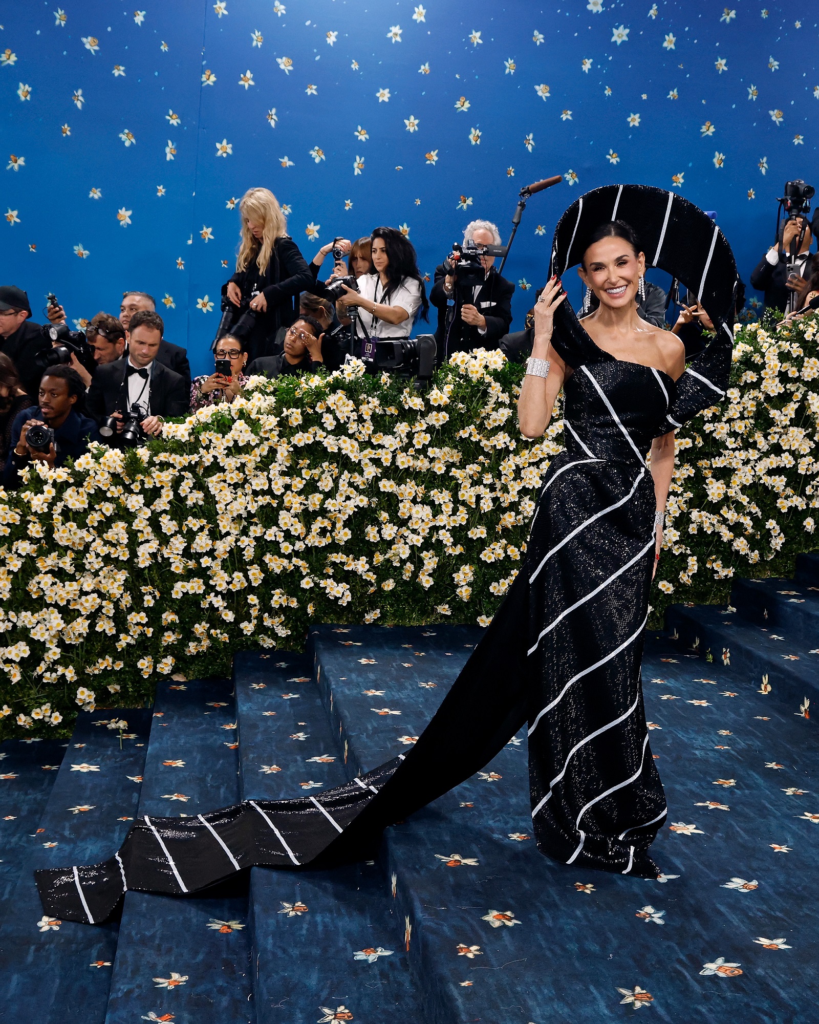 Demi Moore stunned at the Met Gala in a black sequined gown with bold white stripes, featuring a dramatic spiral collar and long matching train. She finished the look with sleek hair and a sparkling diamond bracelet.
