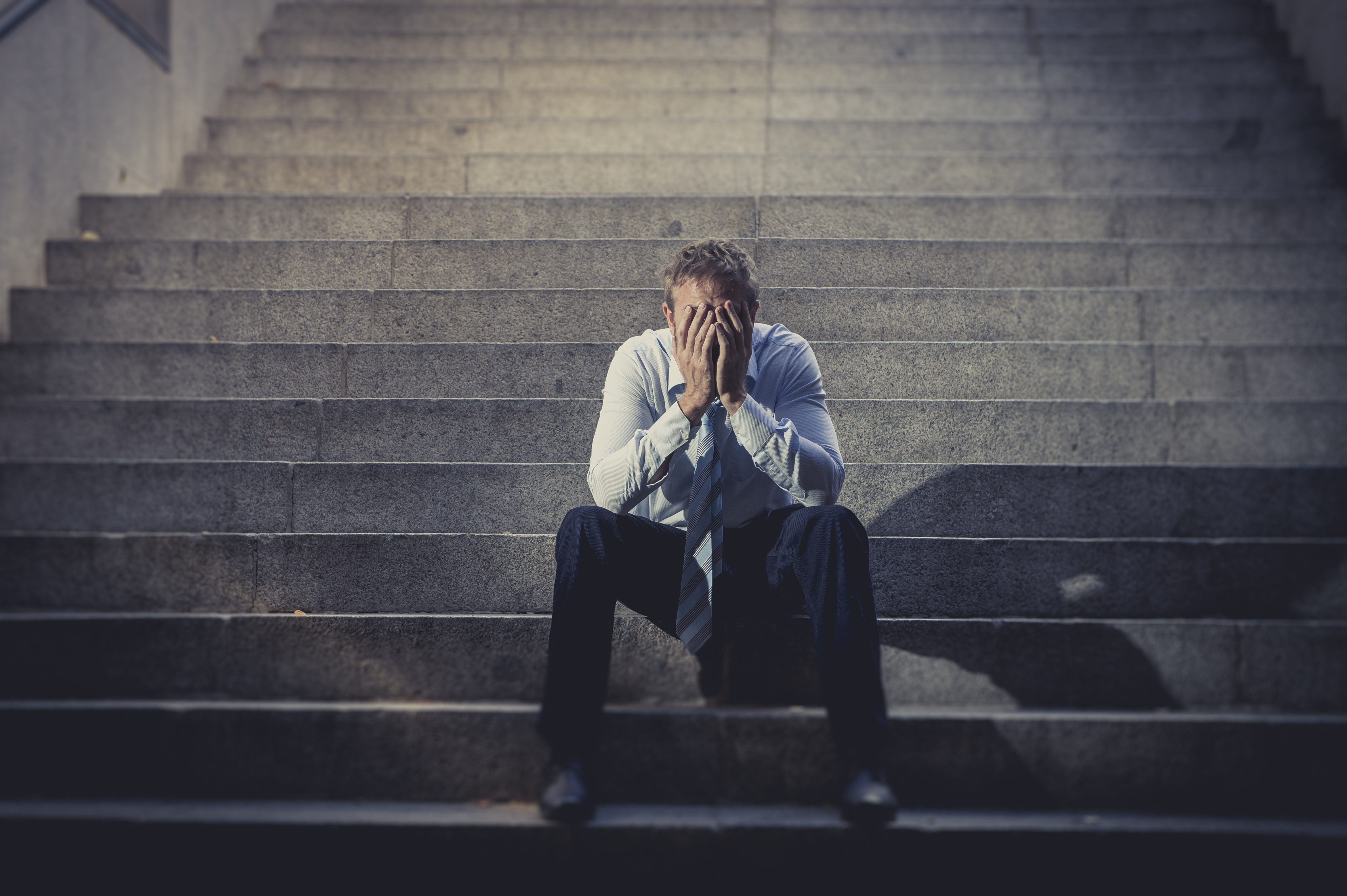 A depressed man sitting on concrete stairs | Source: Shutterstock