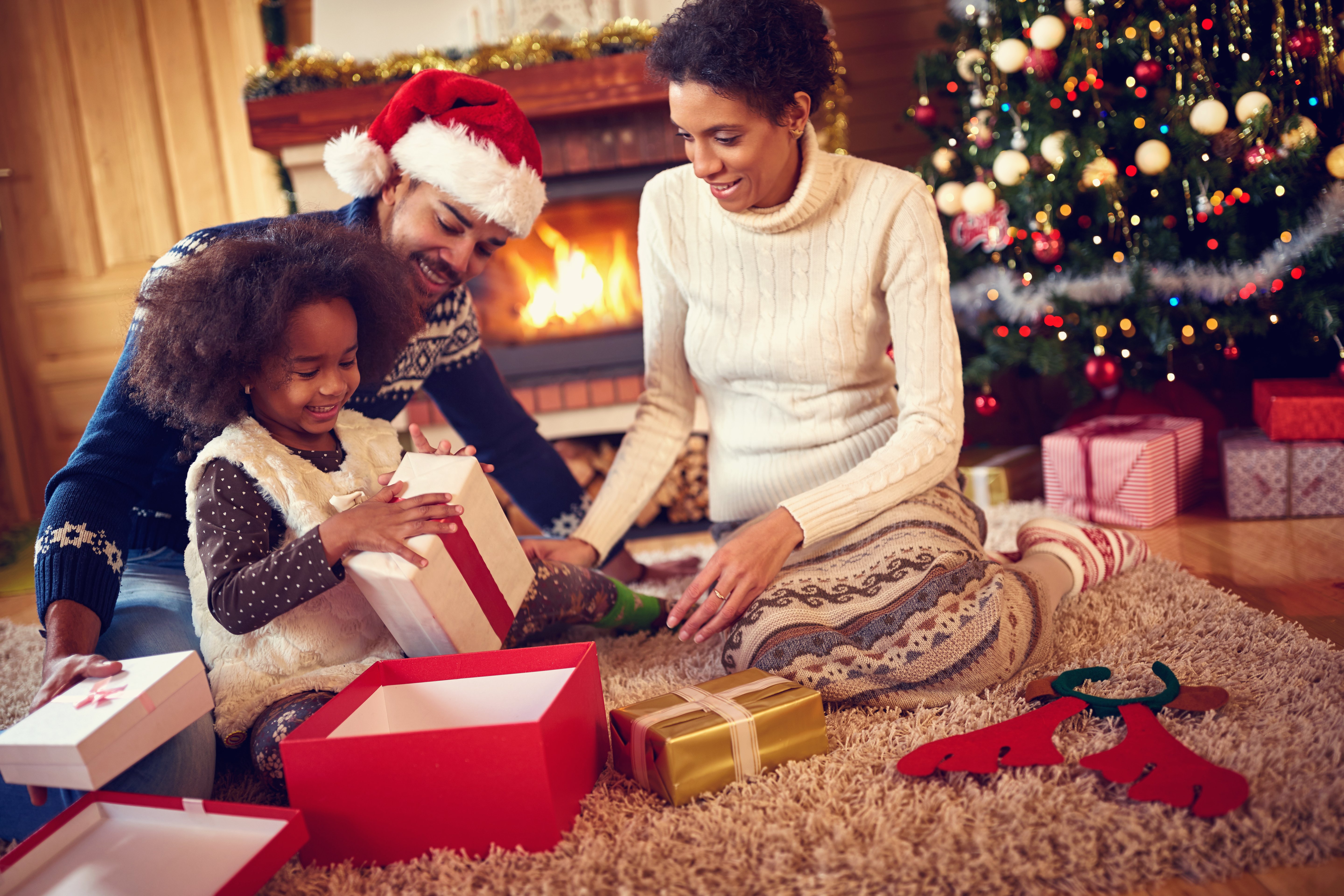 Glückliche Familie am Weihnachtsmorgen, die Geschenke zu Hause vor dem Weihnachtsbaum auspackt | Quelle: Shutterstock
