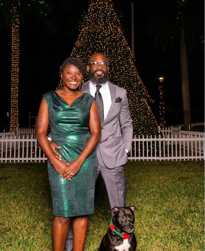 Nancy Metayer Bowen stands in front of her husband, Stephen Bowen, as they pose outdoors at night in formal attire, with a large, brightly lit Christmas tree glowing behind them and their dog sitting calmly at their feet. | Source: Instagram/nancymetayerbowen