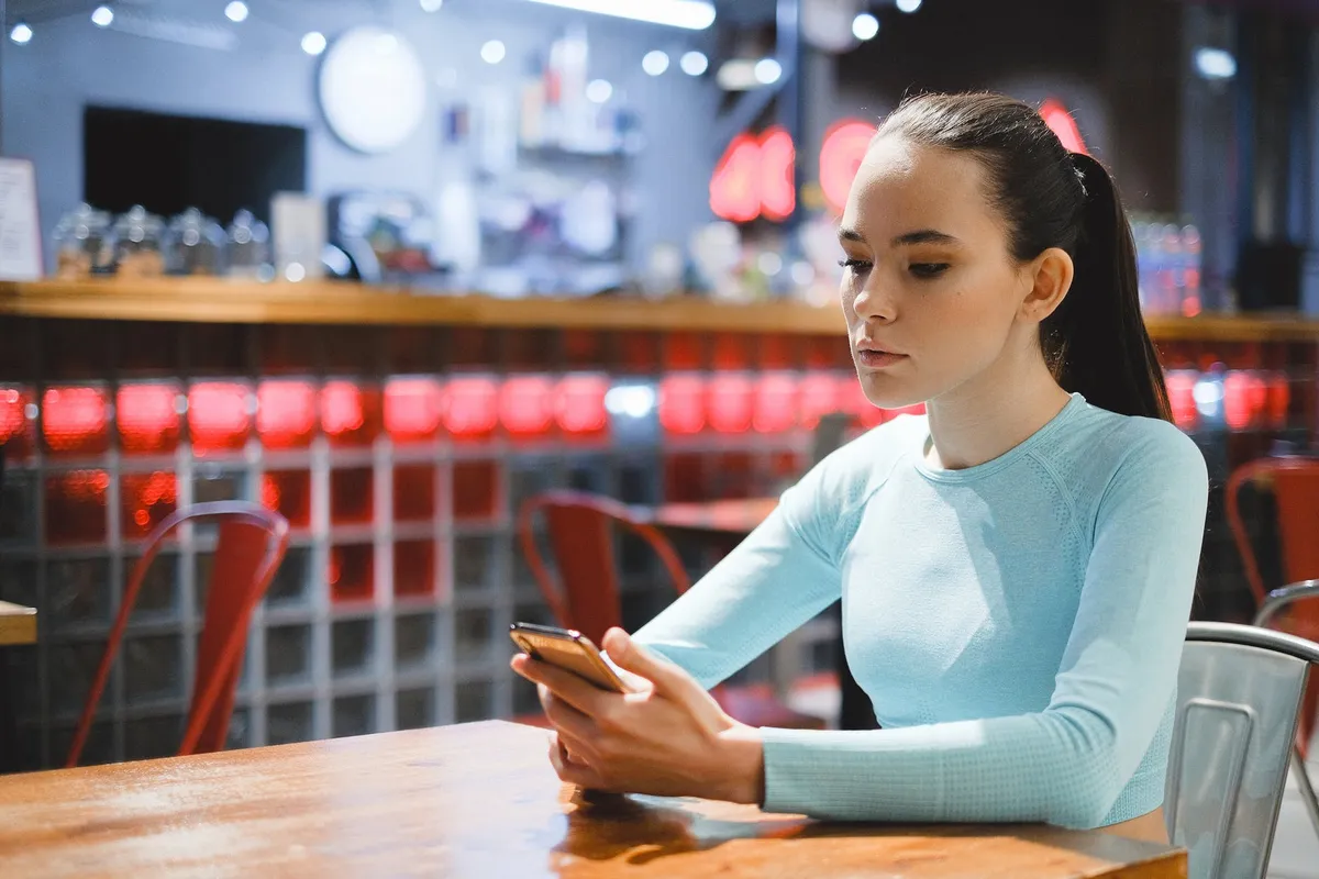 Jeune femme regardant son téléphone portable dans un café | Source : Pexels