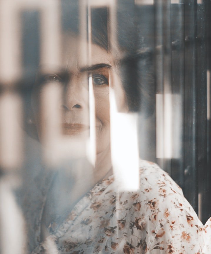 Una anciana elegante mira a través de una ventana. | Foto: Pexels