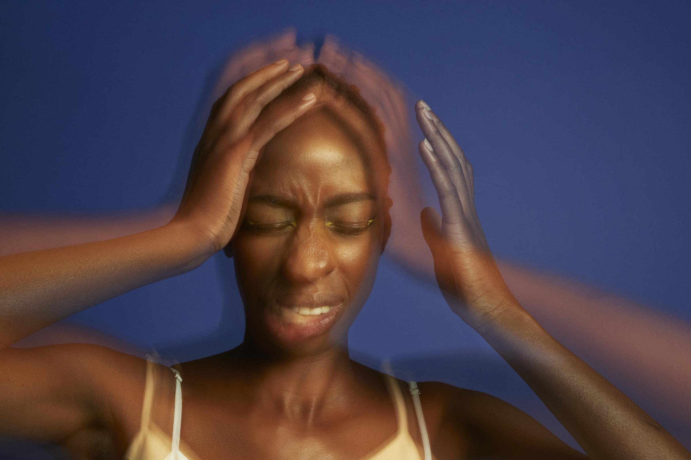 Multiple exposure image of a young woman with a headache, holding her head in her hands and eyes closed | Source: Getty Images