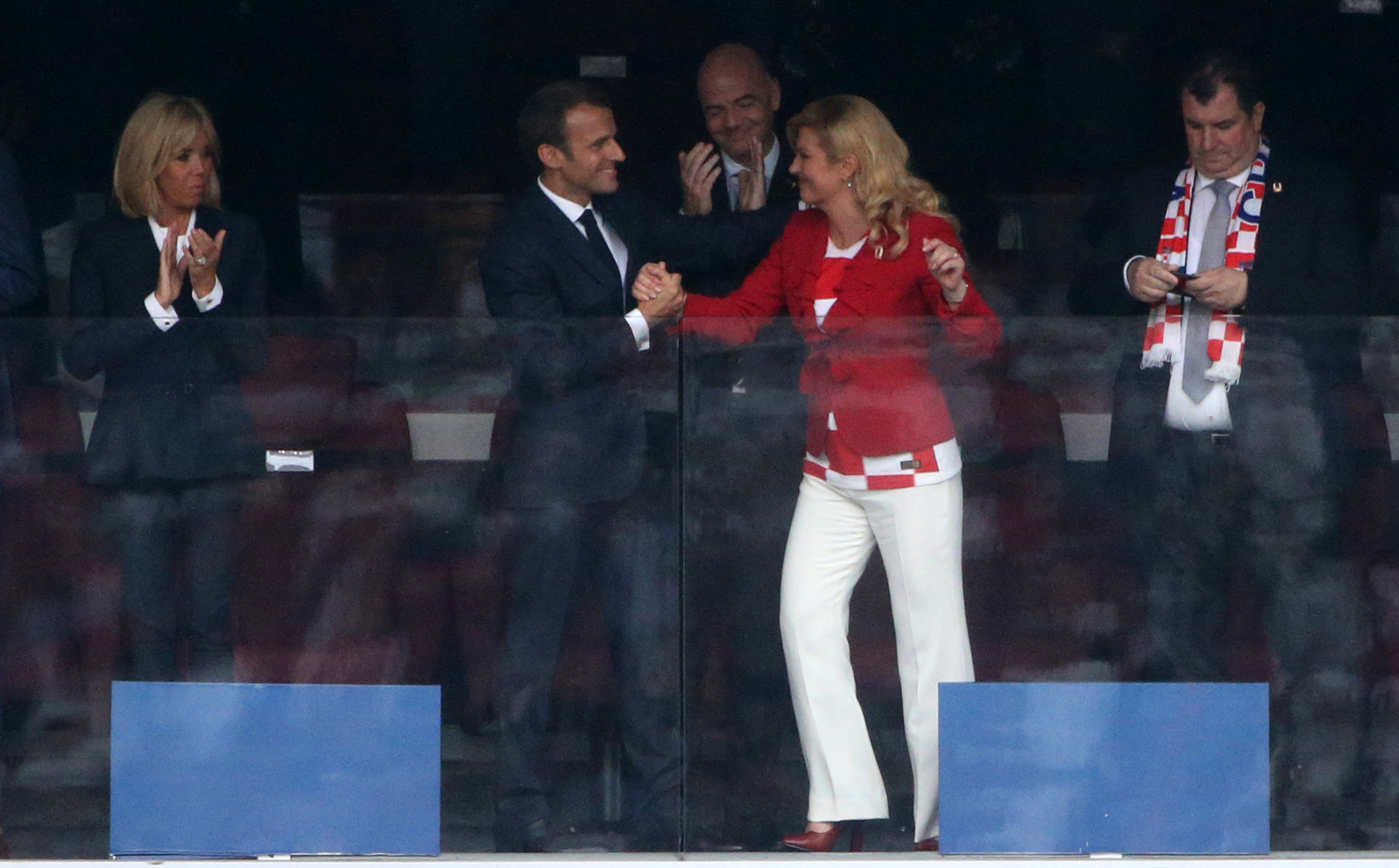 Emmanuel Macron and Kolinda Grabar-Kitarović continue to hold hands and exchange smiles, celebrating in the stands as others applaud around them.