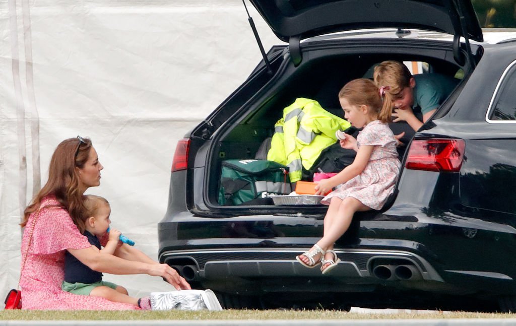 Kate Middleton sits on the grass with Prince Louis while Princess Charlotte and Prince George eat a snack in an SUV at the King Power Royal Charity Polo Match, at Billingbear Polo Club on July 10, 2019, in Wokingham, England | Source: Max Mumby/Indigo/Getty Images