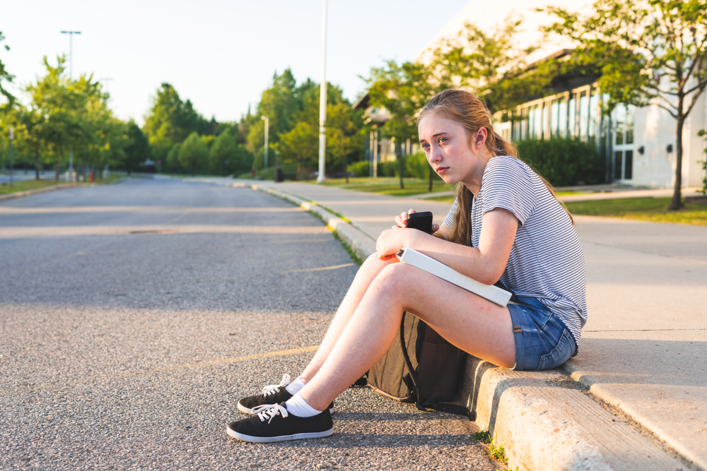 A young girl sitting by the side of a road | Source: Shutterstock
