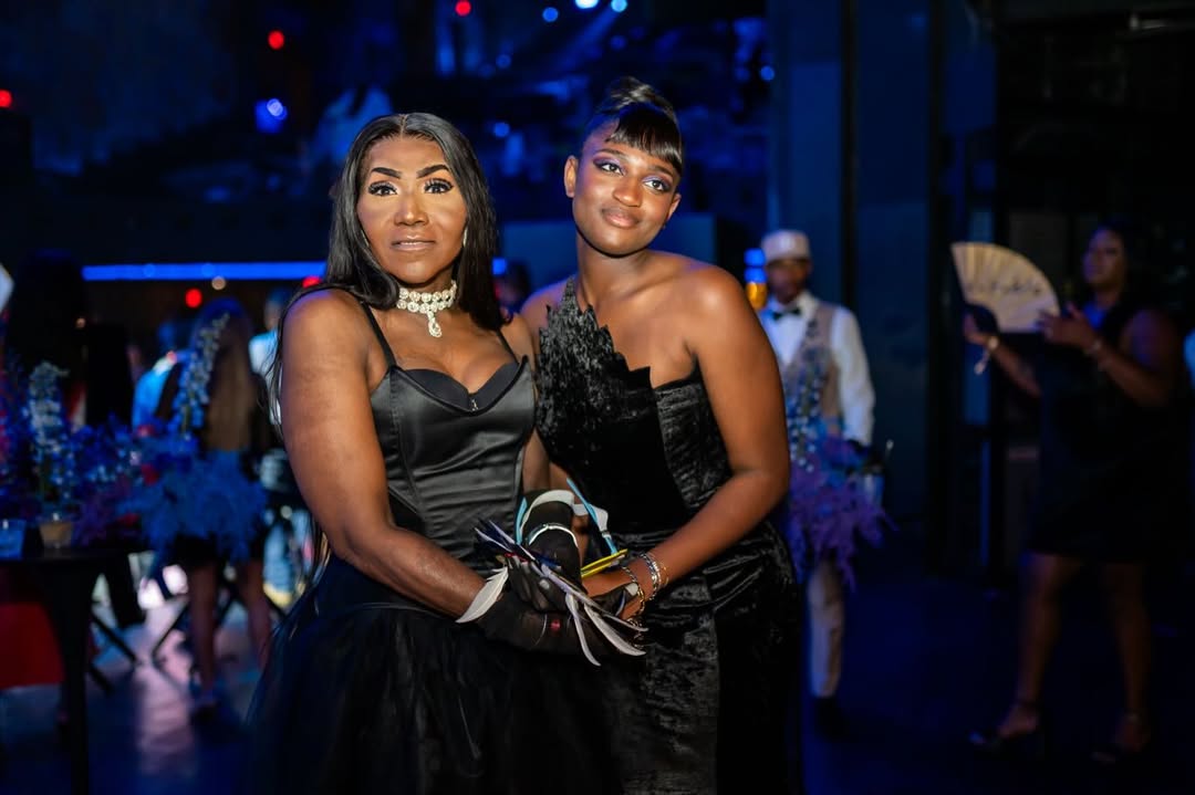 Zaya Wade smiles while posing with Ebony Lane on the event floor, surrounded by guests and illuminated by the venue's blue-toned lighting. | Source: Instagram/translatableproject