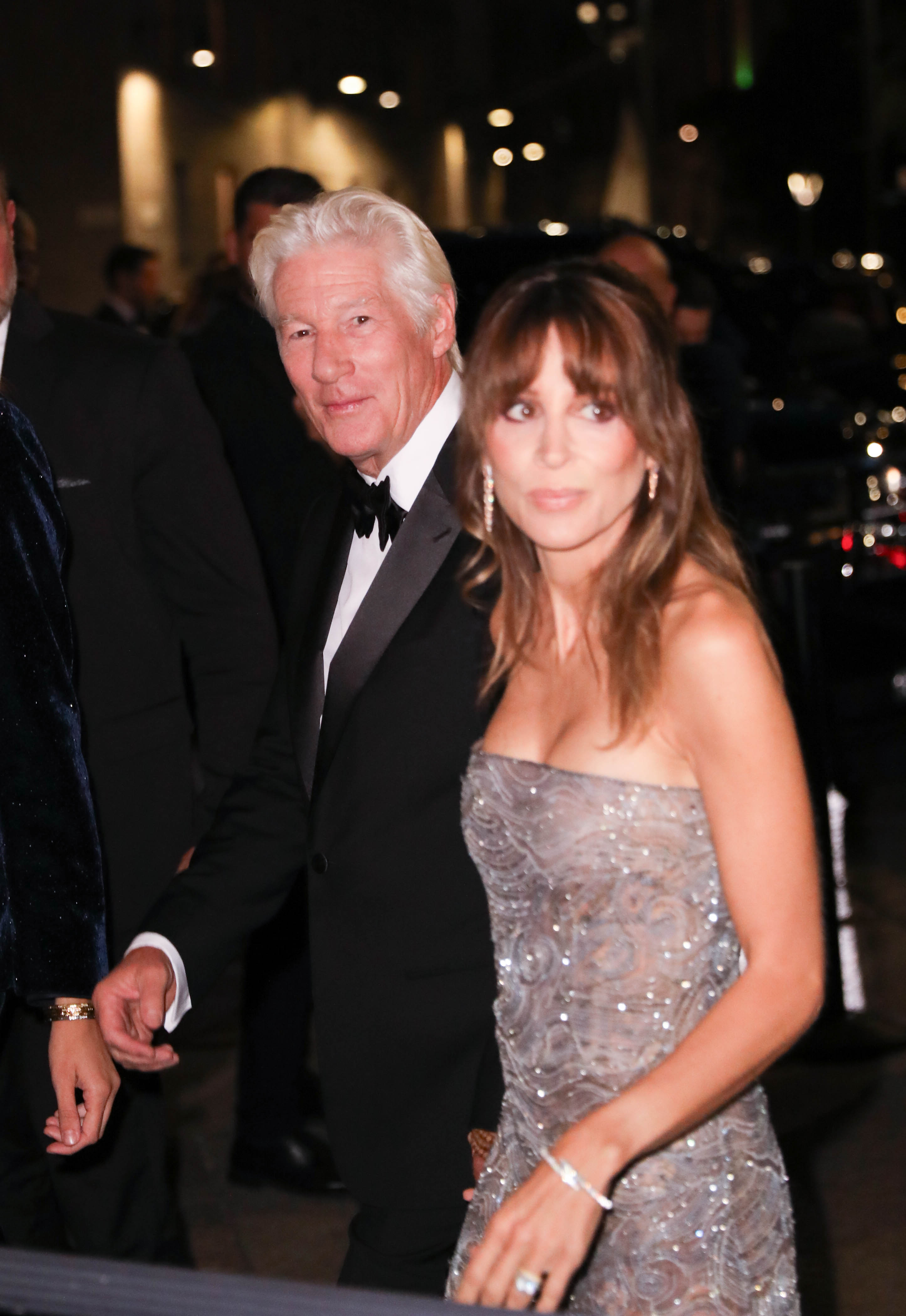 Hand in hand, Richard Gere and Alejandra Silva walk through the crowd — her dazzling silver gown sparkling under the lights, his expression calm and composed.