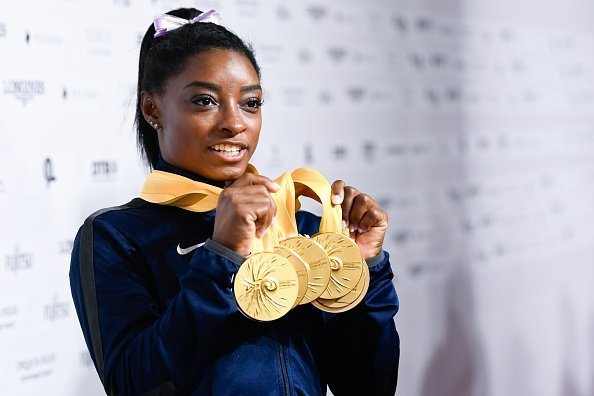 Simone Biles from the USA holding 5 gold medals in her hands.| Photo: Getty Images.