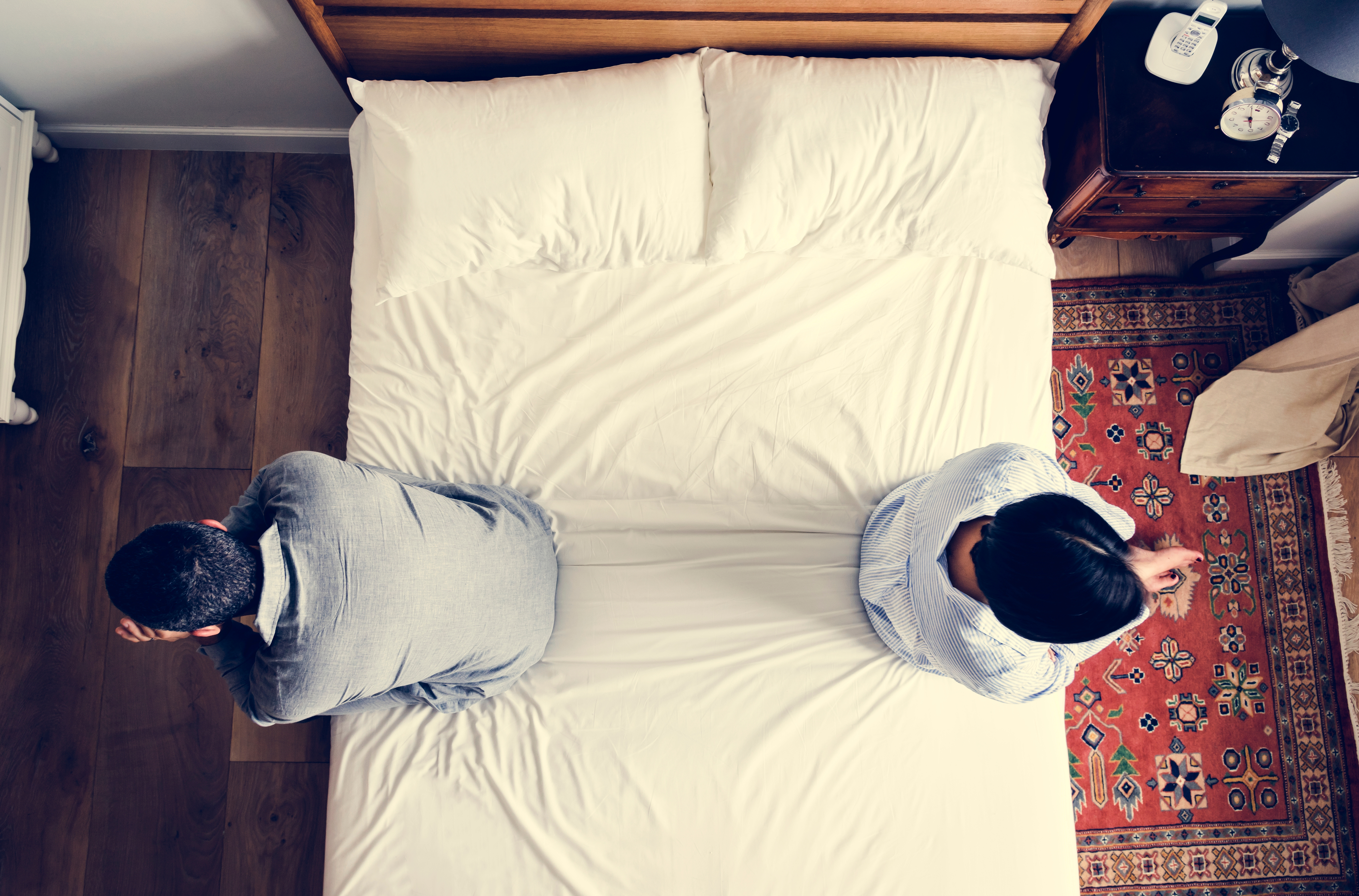 A couple sitting on opposite ends of their bed after an argument | Source: Shutterstock