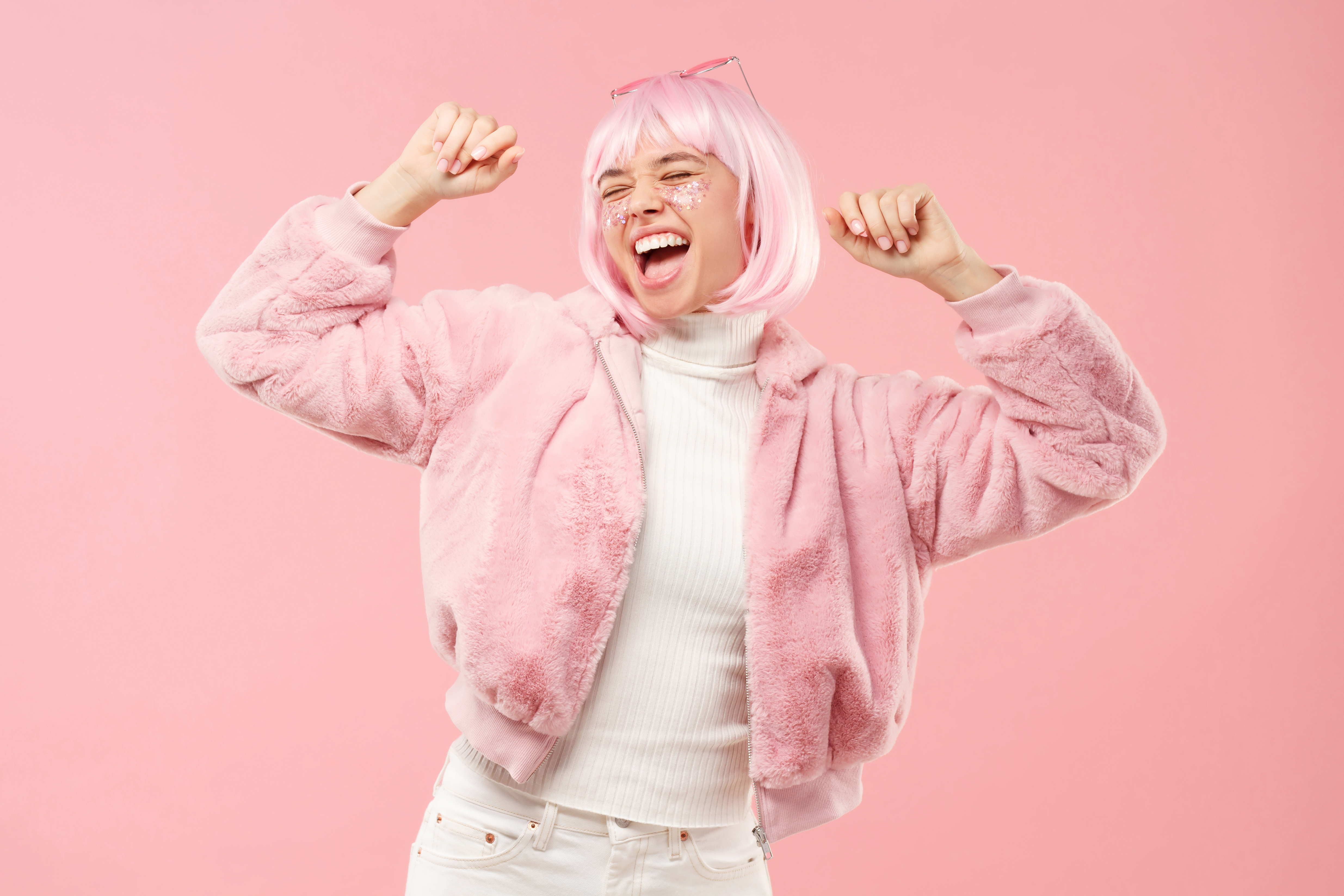 Excited teenage girl dancing and cheering to sounds of music, wearing fluffy fur coat and colored hair at party, isolated on pink background | Source: Getty Images