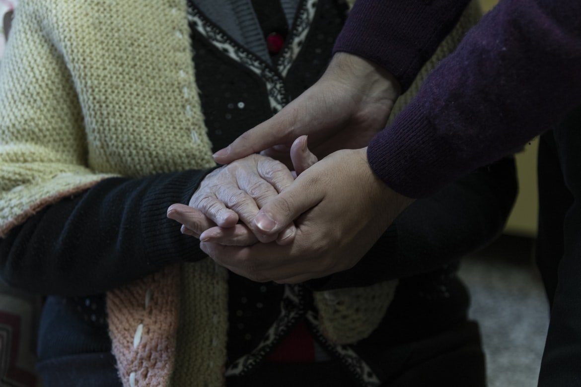 Persona joven sosteniendo las manos de una anciana. | Foto: Unsplash