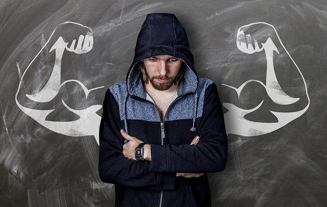 Man in hoodie stands in front of muscled strong arms drawing on board | Photo: Pixabay