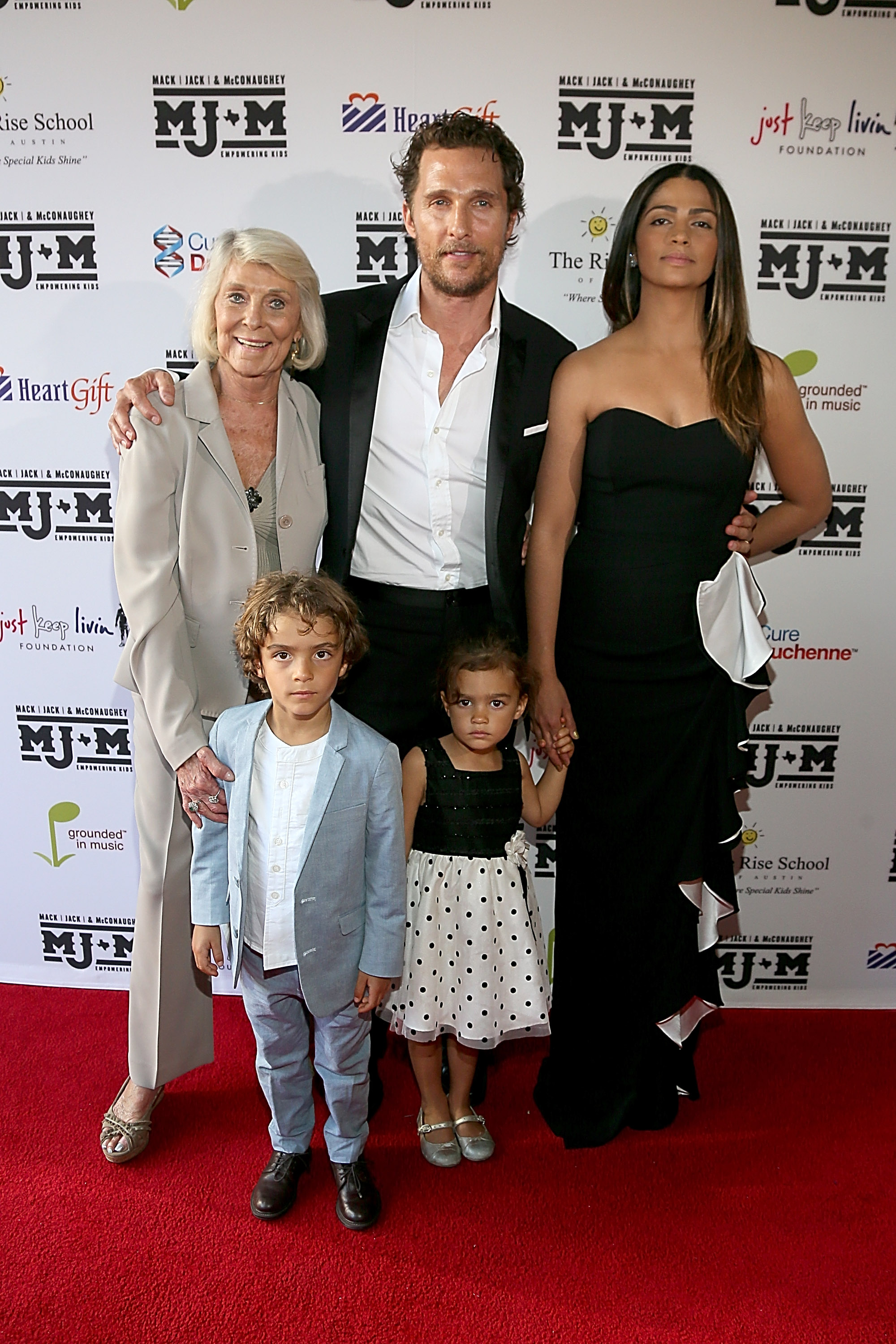 Levi McConaughey stands in front wearing a light blazer and trousers. Vida McConaughey stands beside him in a sleeveless dress. Matthew McConaughey, Camila Alves, and Kay McConaughey stand behind them on the red carpet.