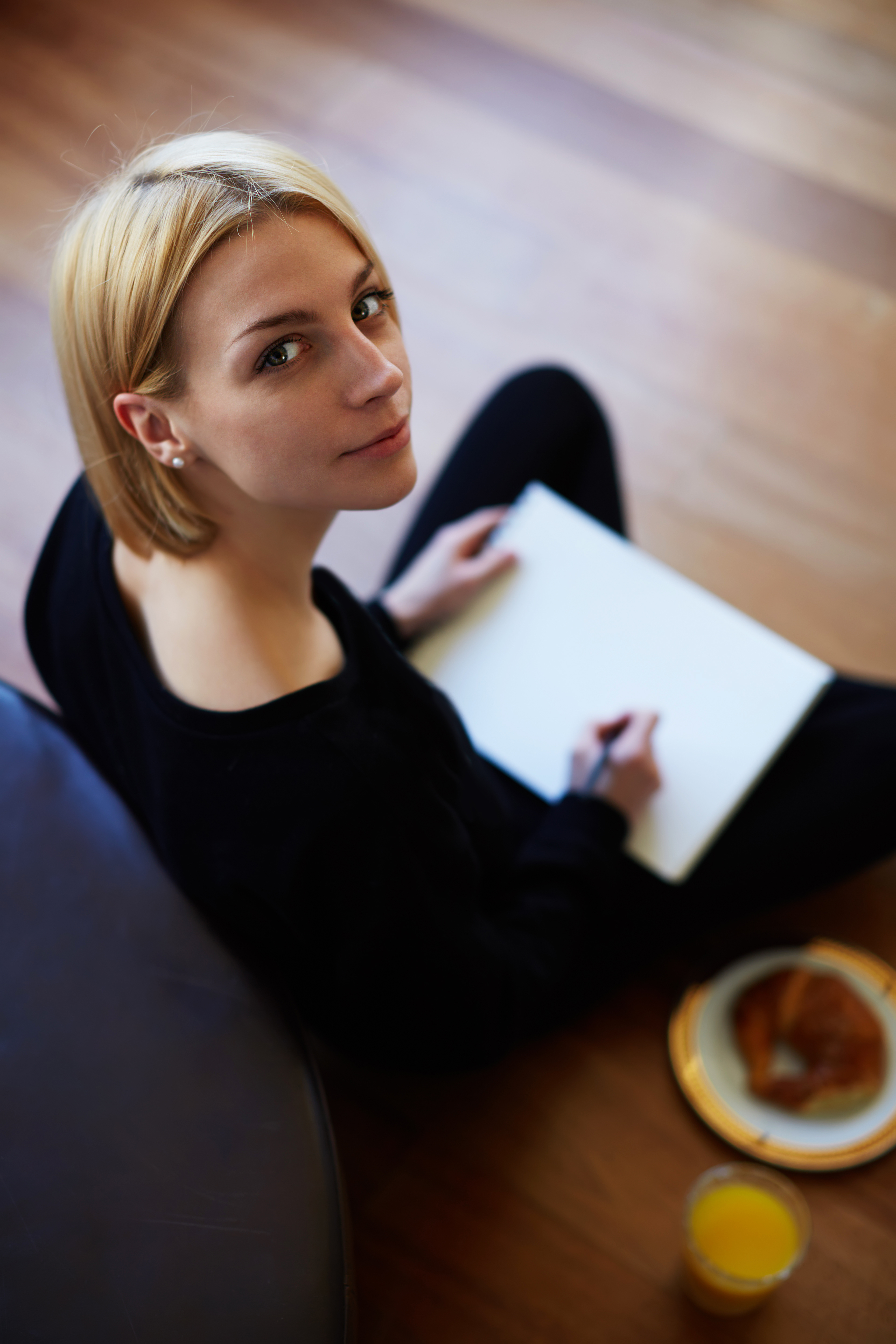 Top view shot of blonde hair young woman drawing on the paper while sitting on the floor of her living room | Source: Shutterstock.com