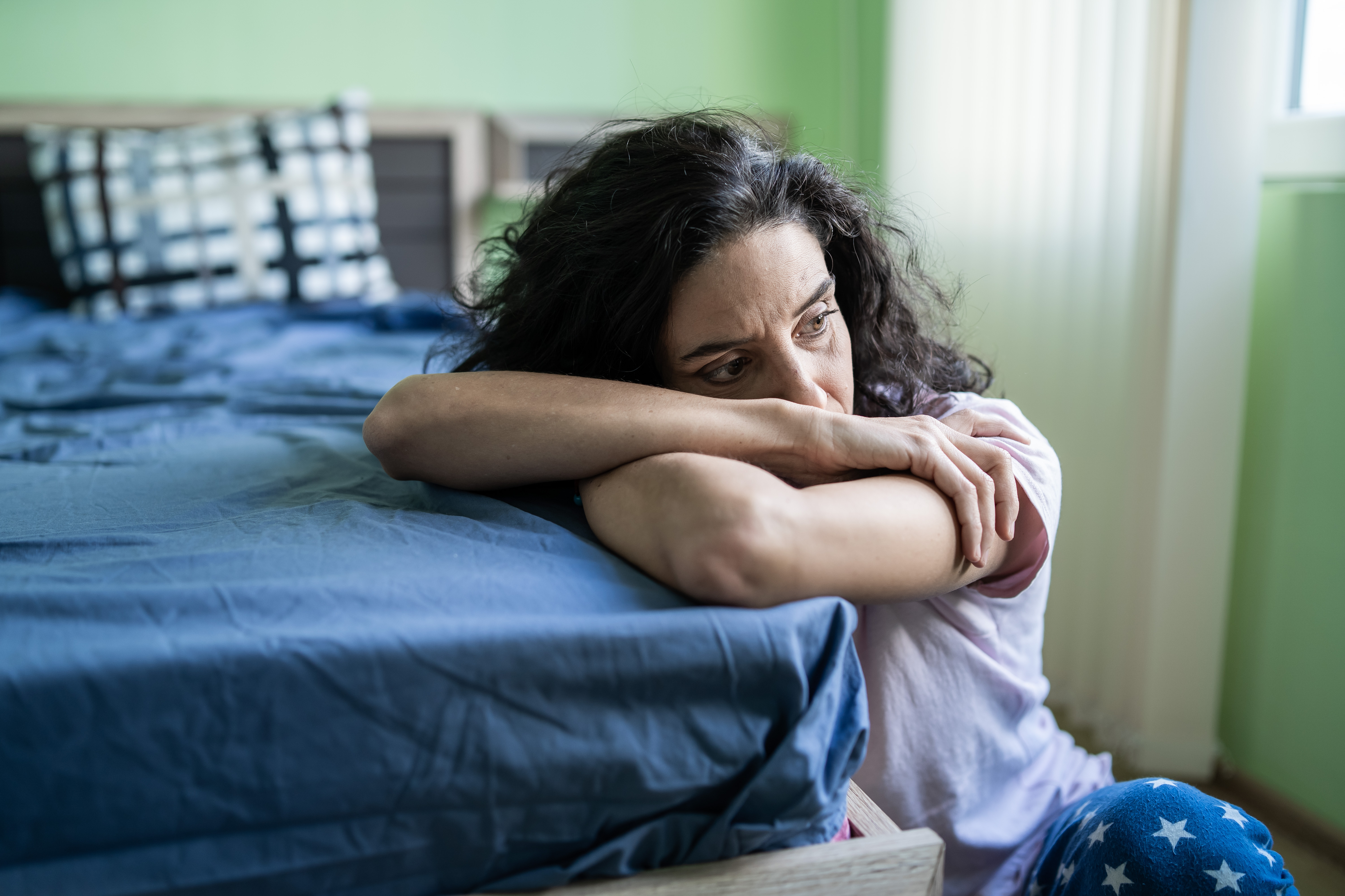 Worried woman sitting on floor next to bed | Source: Getty Images