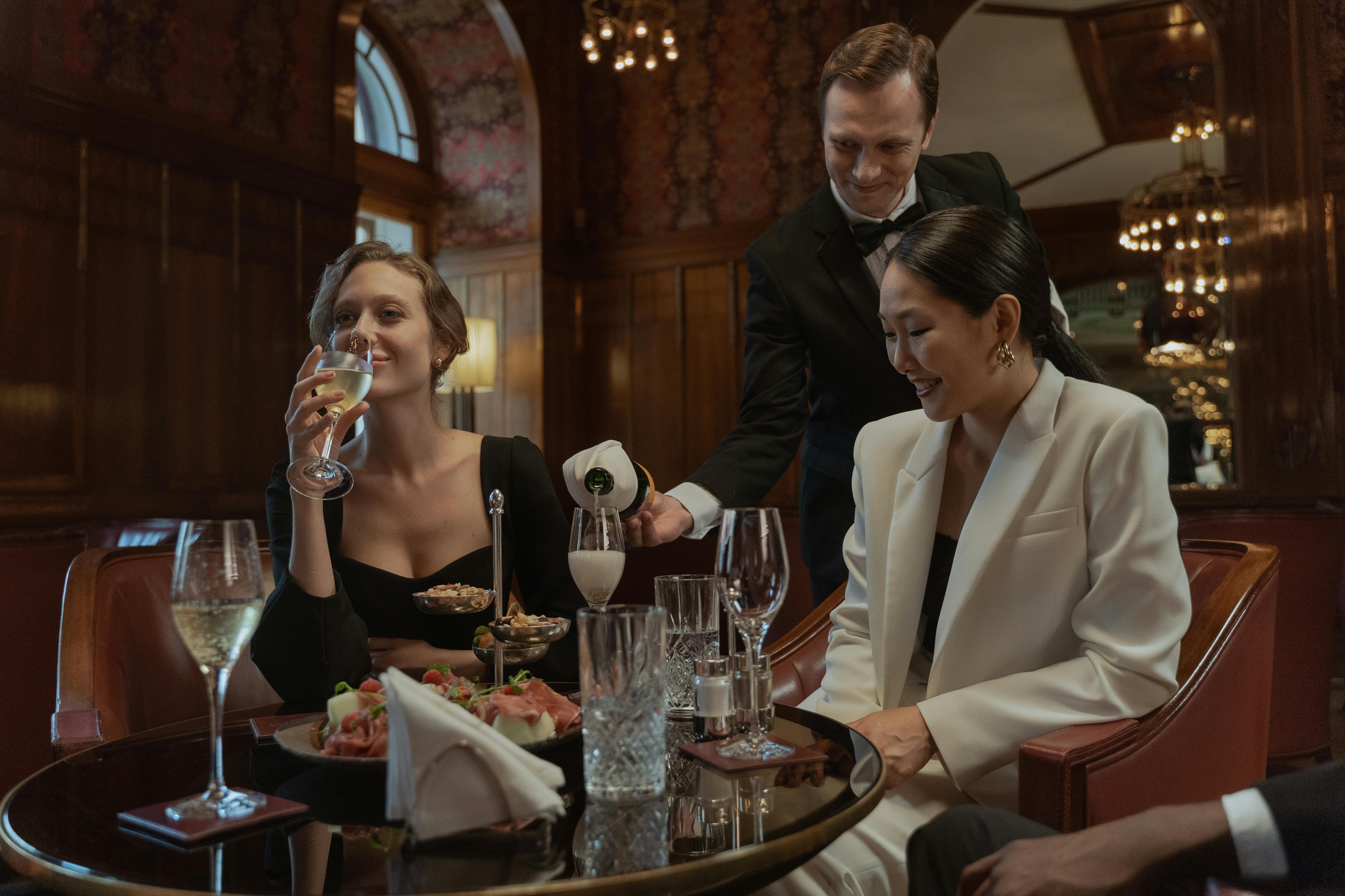Women enjoying drinks while a waiter serves them | Source: Pexels