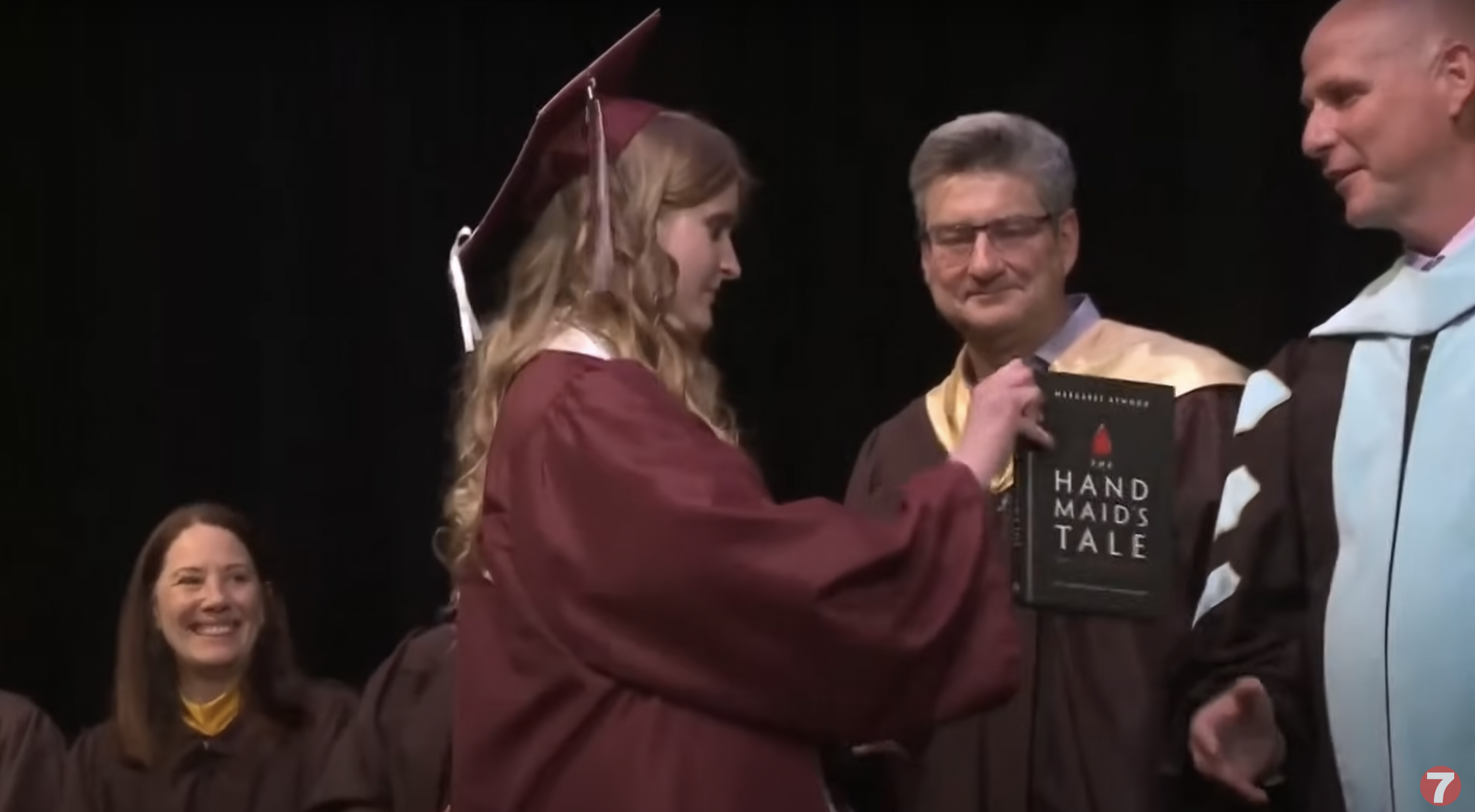 Annabelle Jenkins handing over the graphic novel adaptation of Margaret Atwood's "The Handmaid's Tale" to Superintendent Derek Bub at her graduation ceremony, as seen in a video dated May 29, 2024 | Source: YouTube/ktvb7