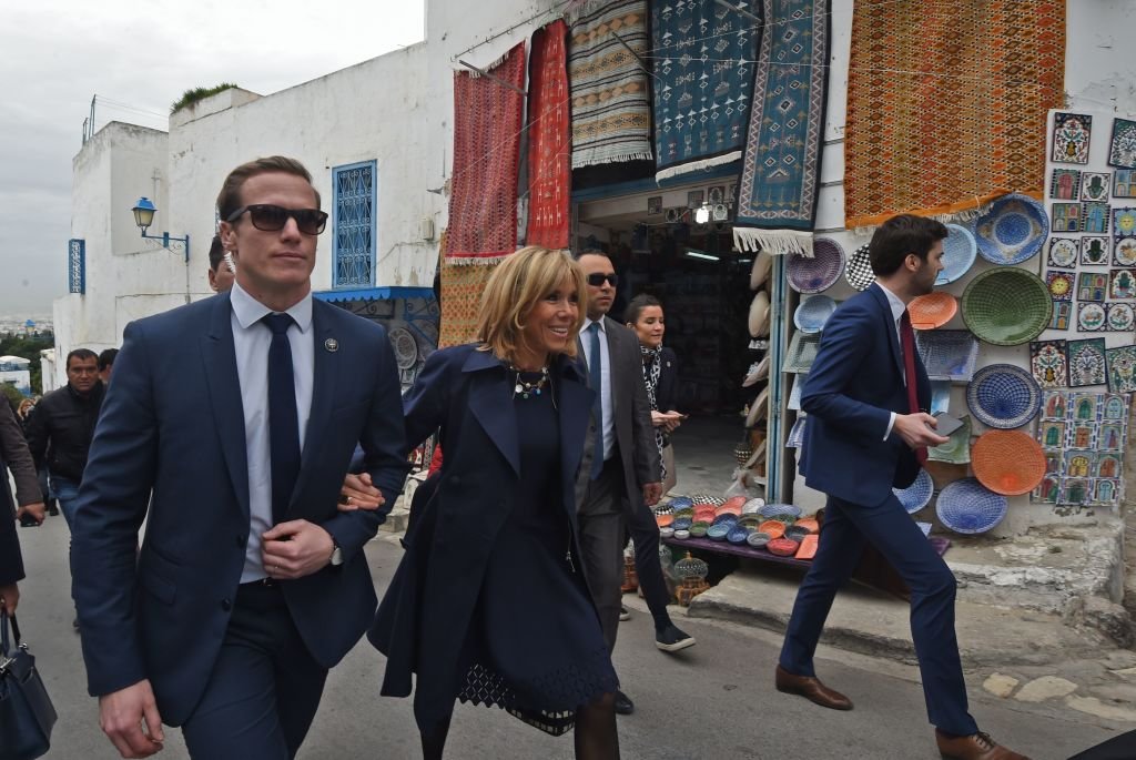 Brigitte Macron est escortée par un membre de sa garde rapprochée lors d'une visite dans la ville de Sidi Bou Said, près de Tunis, le 1er février 2018. | Photo : Getty Images
