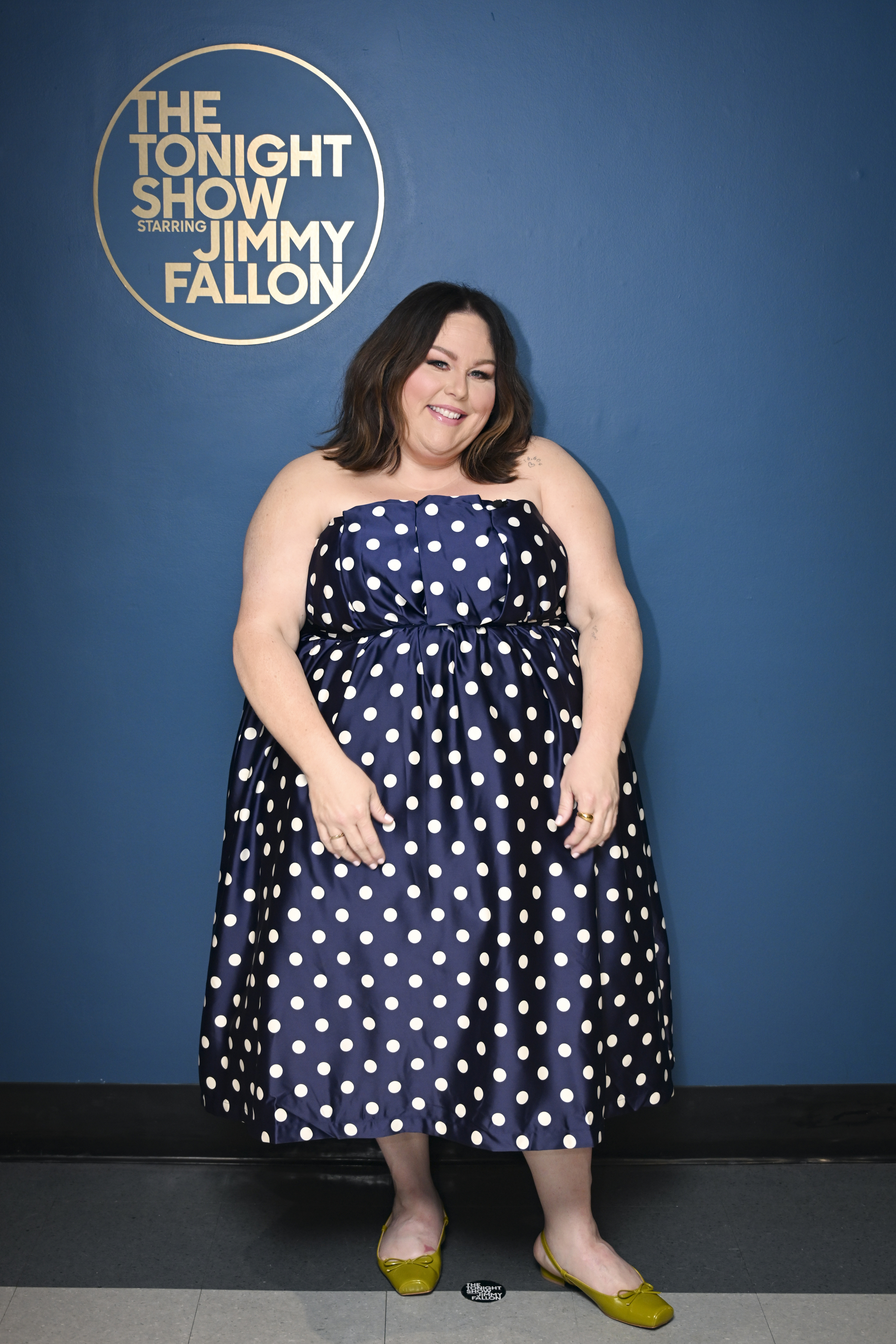 Metz posed backstage at "The Tonight Show Starring Jimmy Fallon" in a navy polka-dot midi dress with yellow flats. The photo shows a later stage of her transformation after she began using a GLP-1.