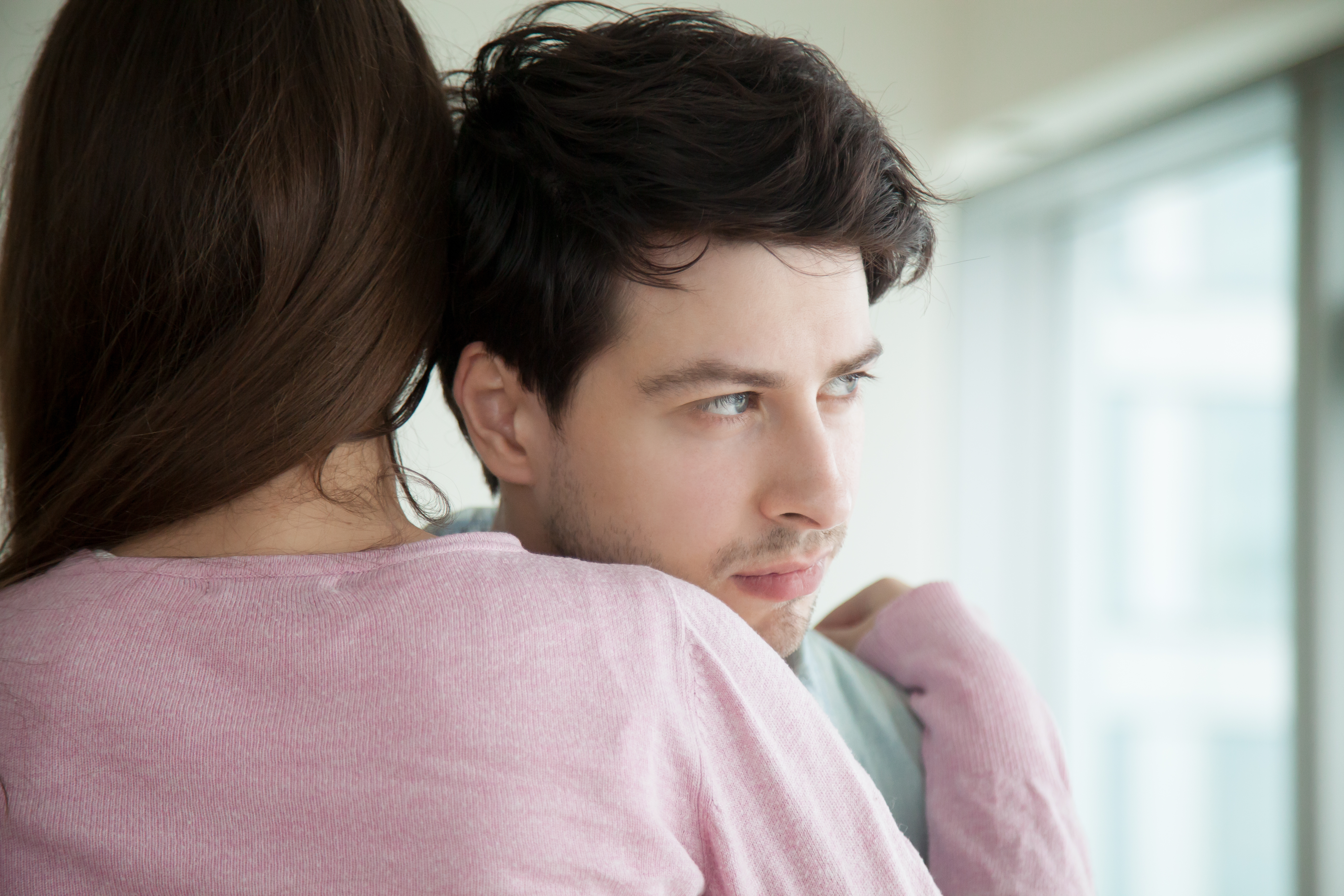 A man looks away through the window while his girlfriend hugs him for support | Source: Shutterstock
