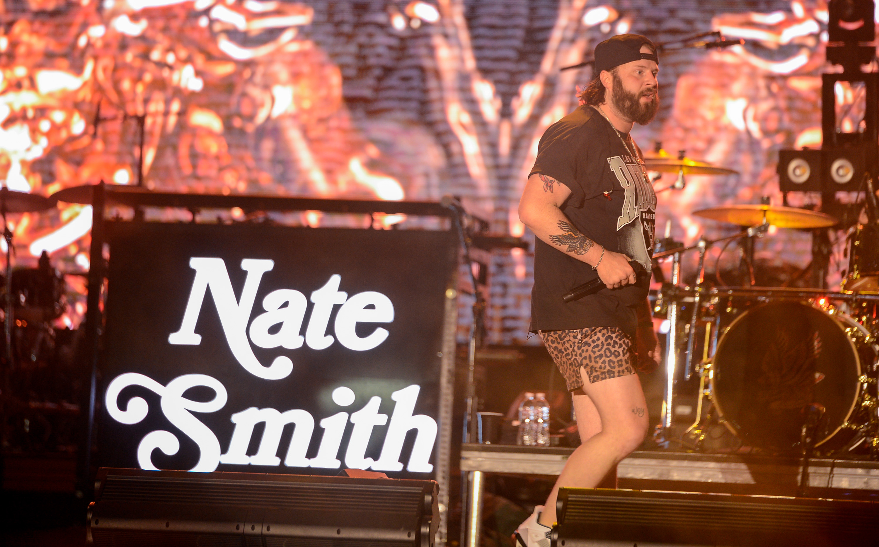 Nate Smith brings a playful twist to his festival performance, taking the stage in a graphic T-shirt, leopard-print shorts, and white sneakers as his name glows prominently behind him.
