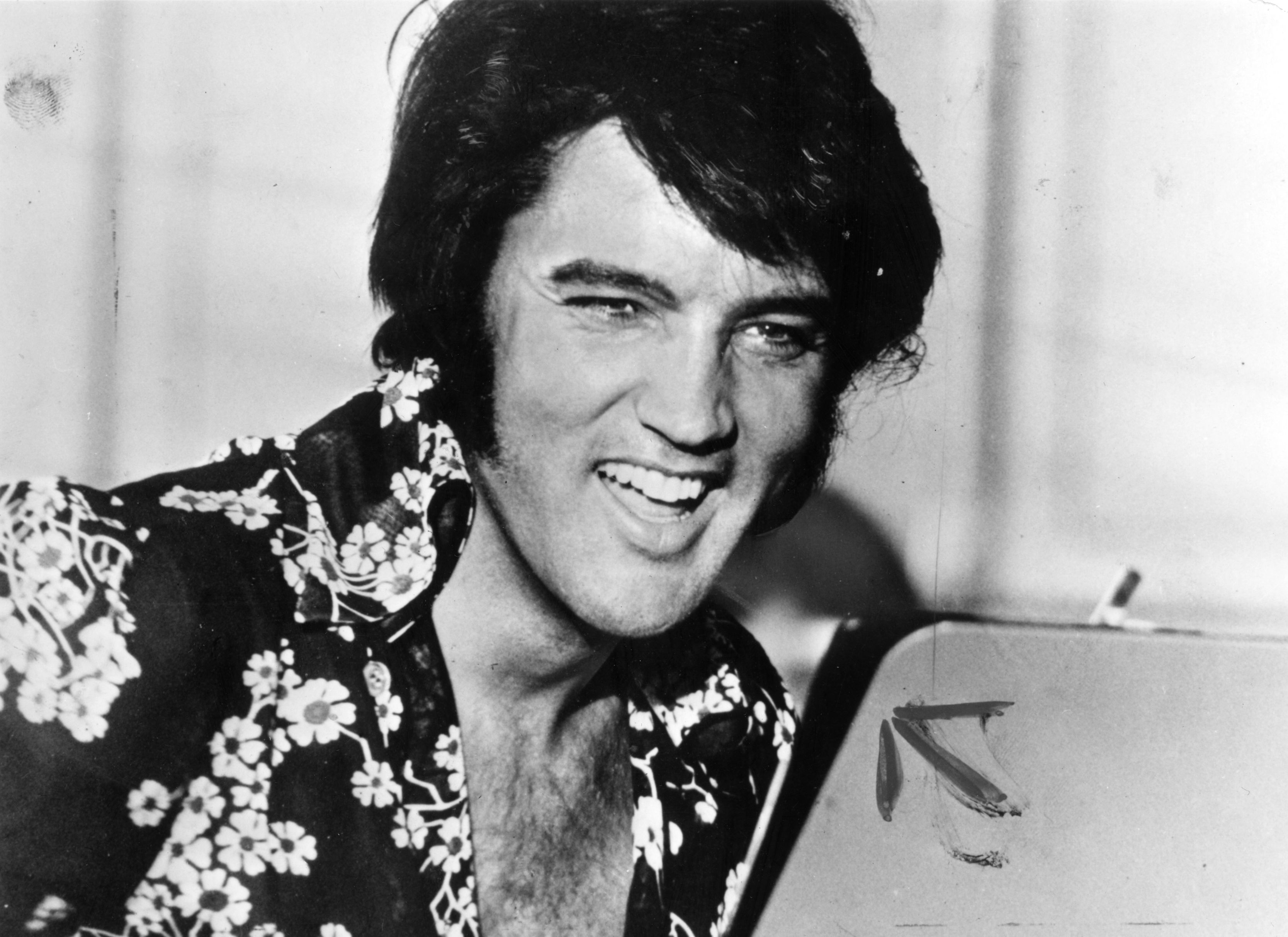 Elvis Presley laughing while posing in a black-and-white image circa 1975. | Source: Keystone/Getty Images