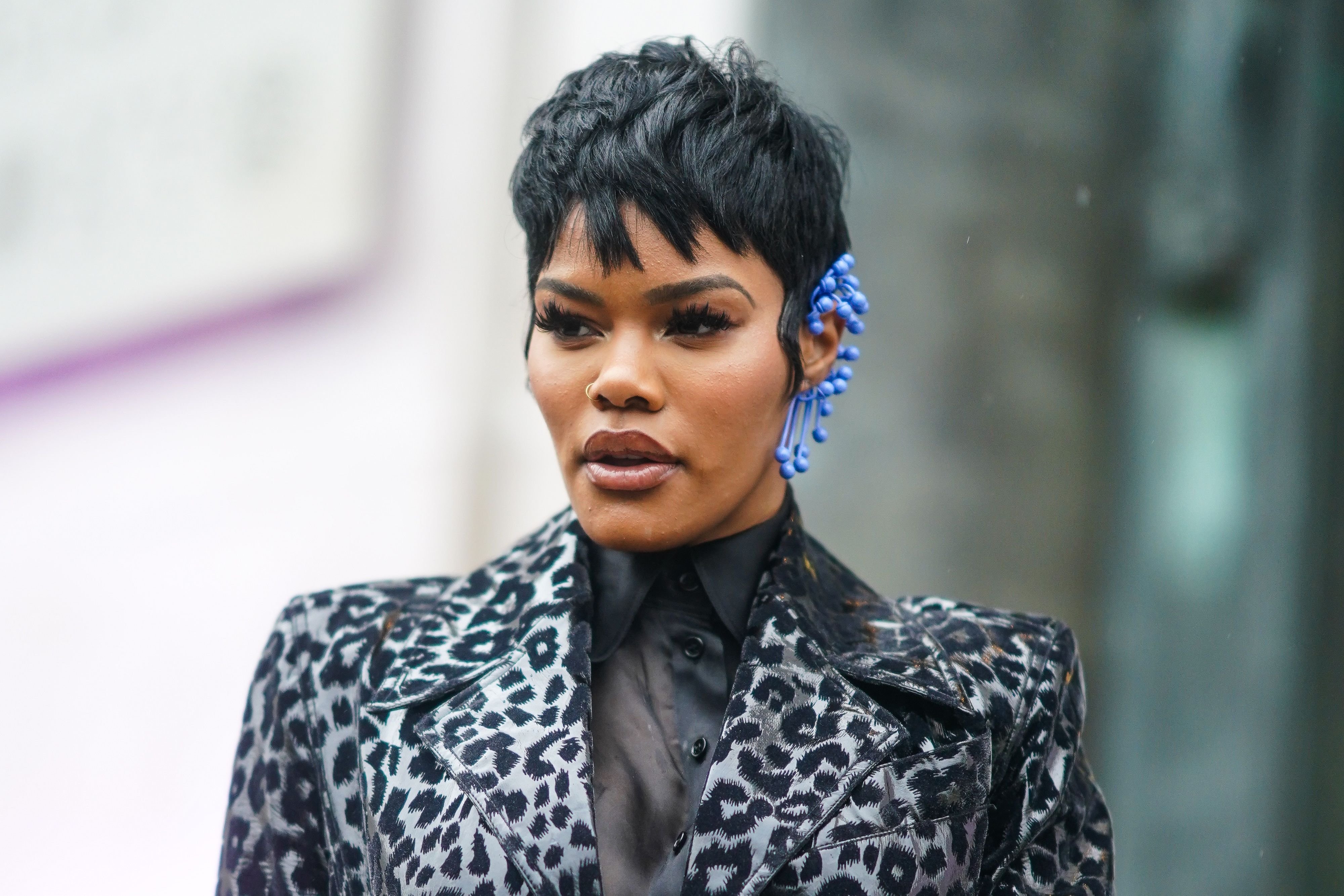 Teyana Taylor wears a black shirt, a long black and gray leopard print trench coat and a blue earring outside Mugler at Paris Fashion Week on February 26, 2020 | Photo: Getty Images