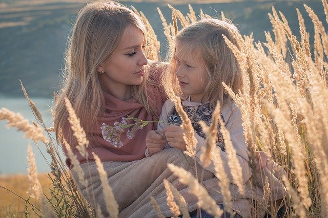 Woman sits with young girl in a meadow | Photo: Pixabay