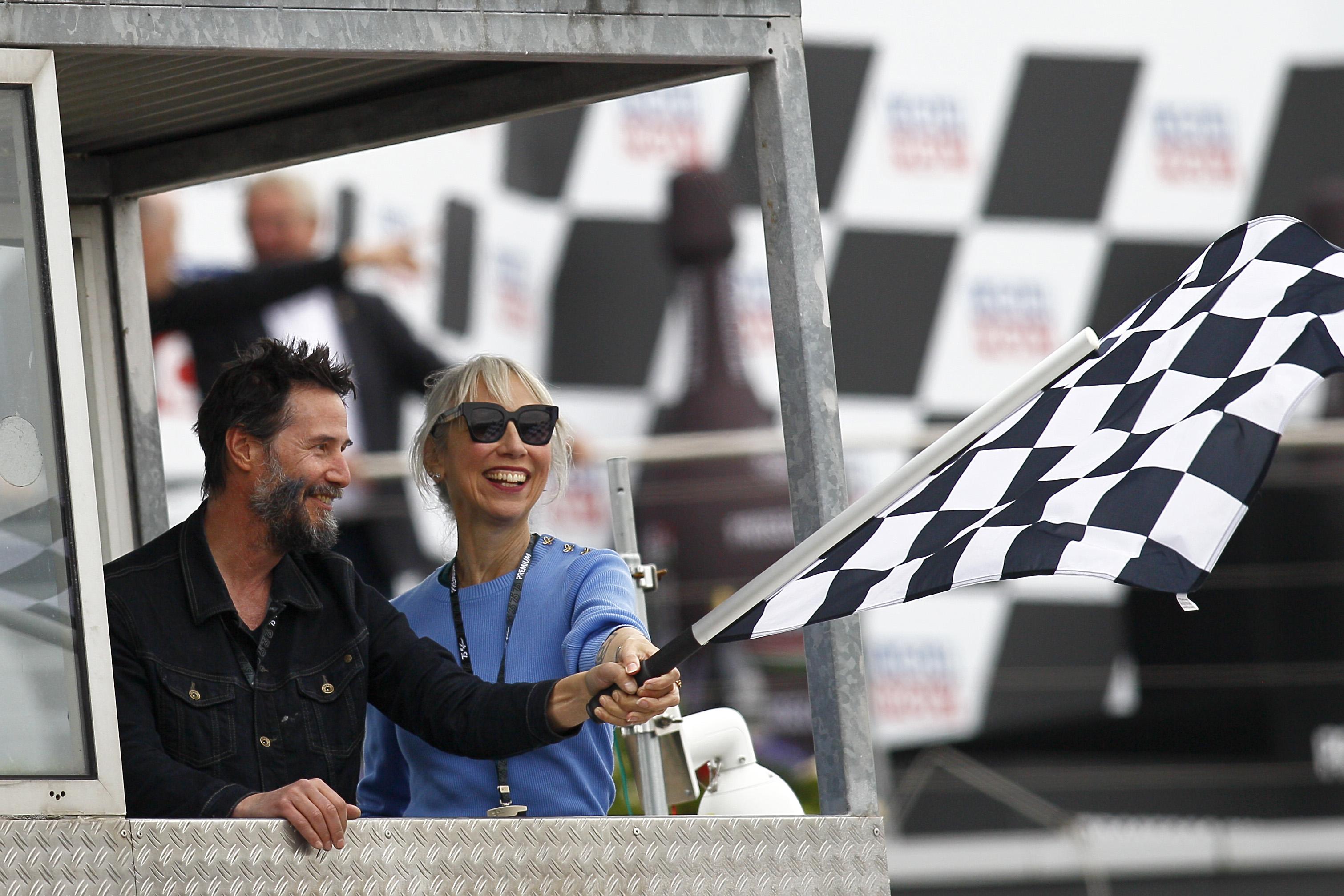 Keanu Reeves and Alexandra Grant smile as they wave the checkered flag at the Liqui Moly Motorrad Grand Prix Deutschland at Sachsenring Circuit in Hohenstein-Ernstthal, Germany on July 7, 2024. | Source: Getty Images