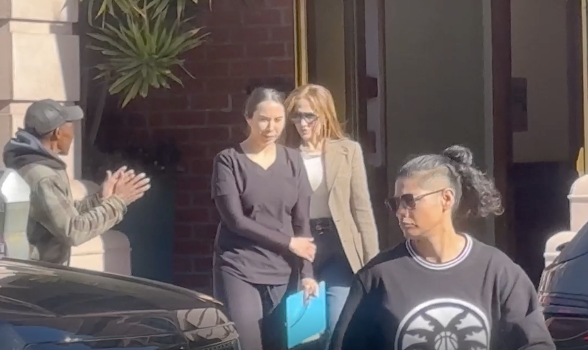 Jennifer Lopez exits the building with others as a homeless man clasps his hands nearby | Source: YouTube/TMZ