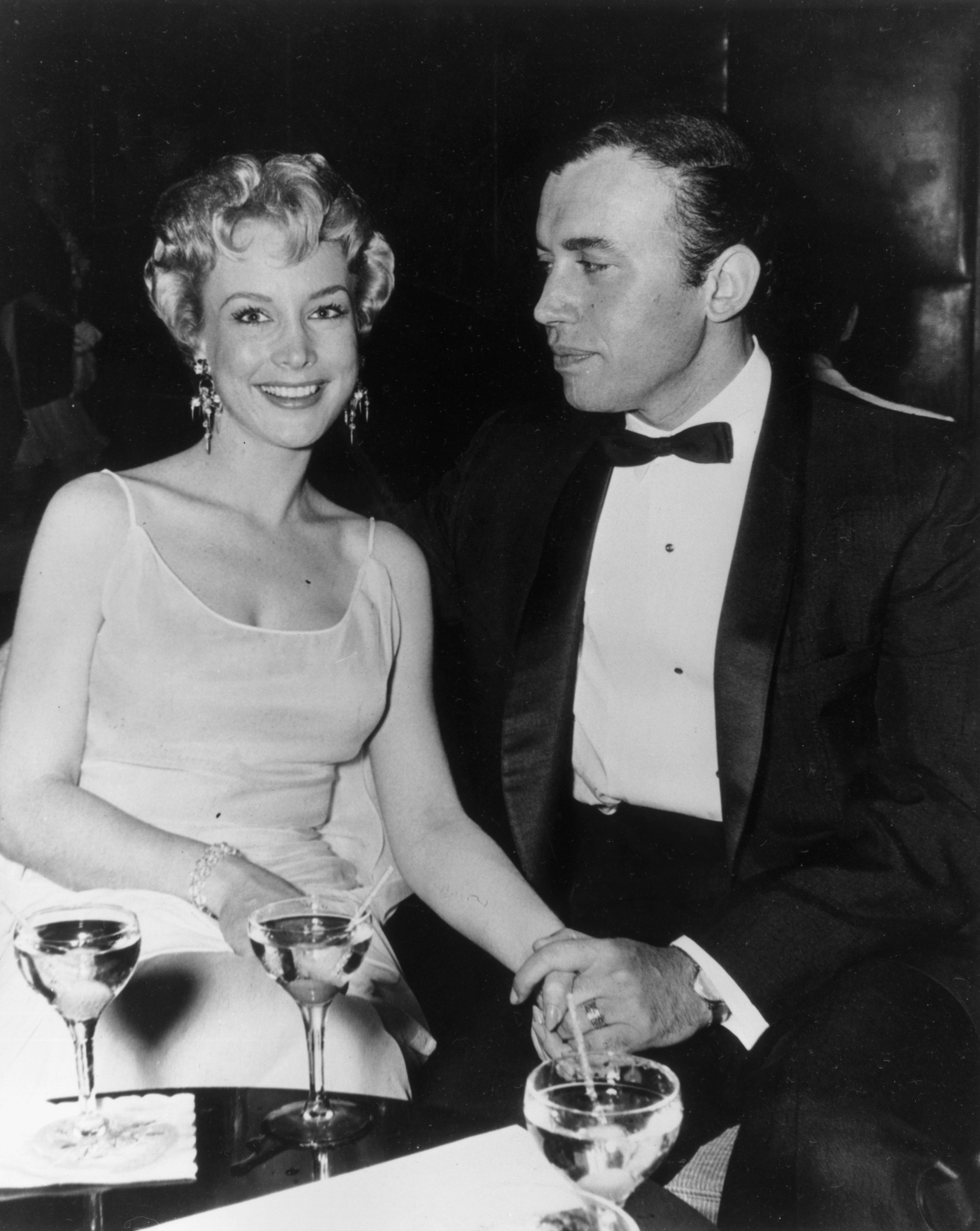 Barbara Eden and Michael Ansara holding hands while seated at a table with cocktails in formal attire circa 1965 | Source: Getty Images 