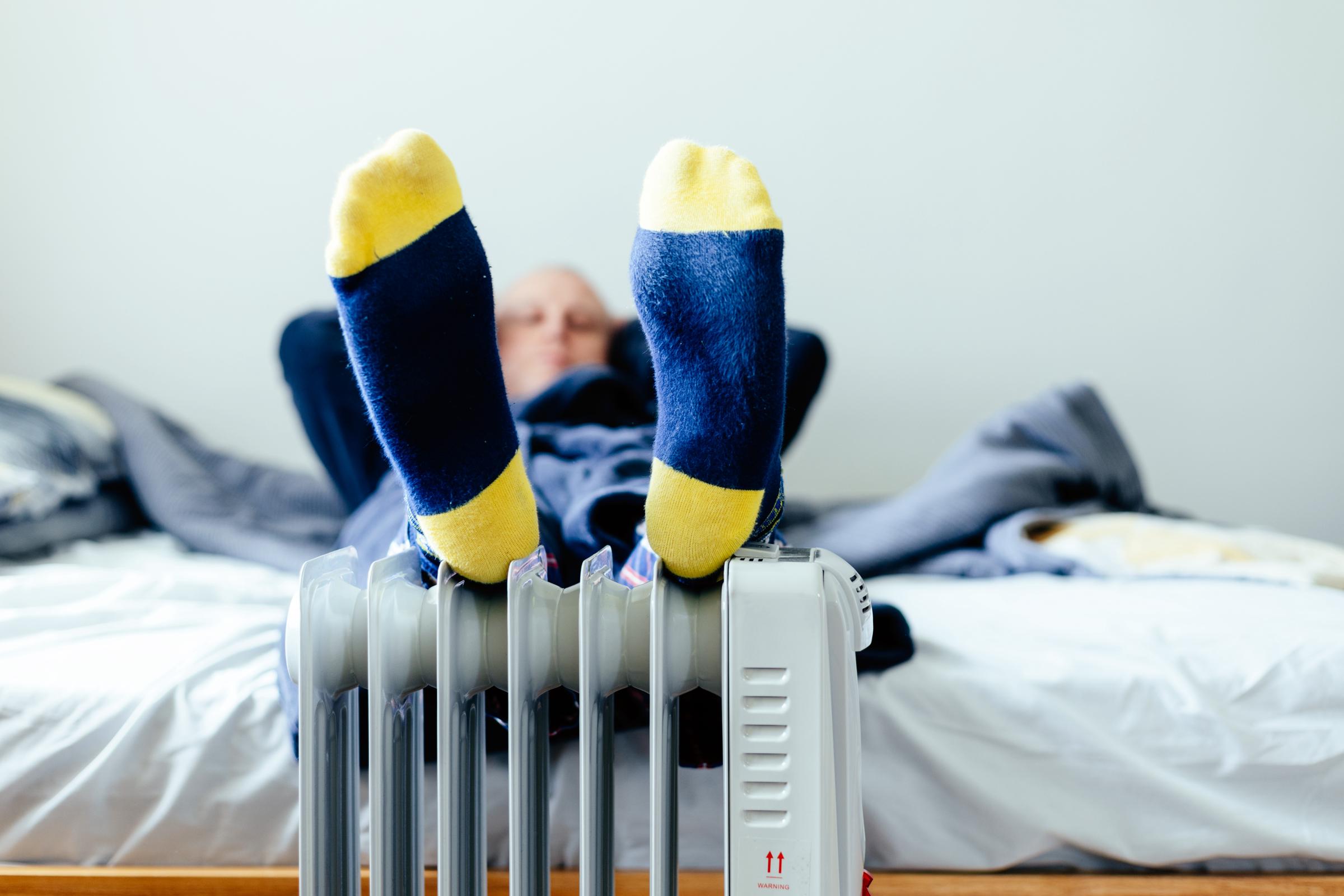 A man resting his feet on an electric heater with socks on | Source: Getty Images