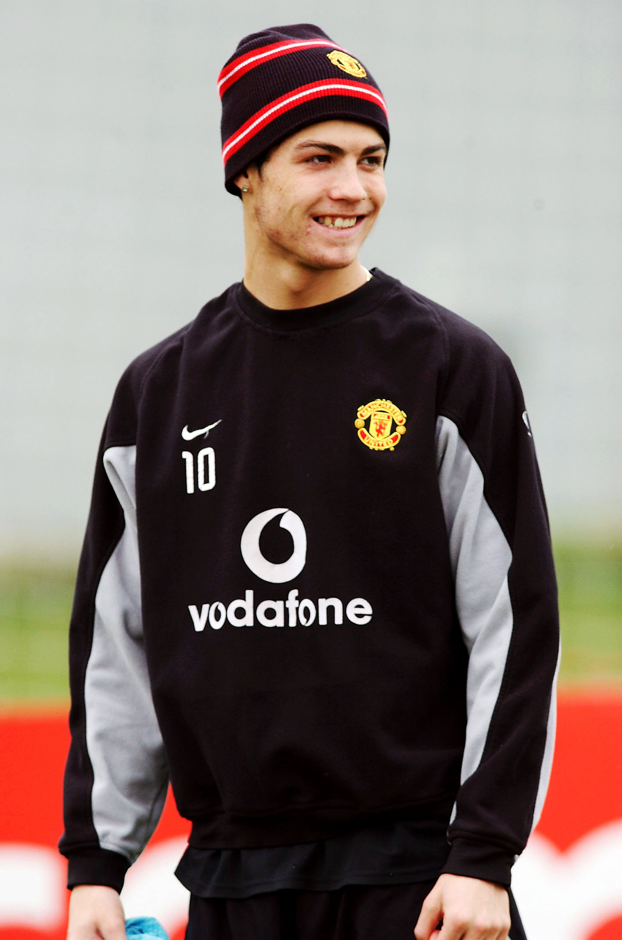 Cristiano Ronaldo smiled during Manchester United's first-team training session at Carrington on March 26, 2004. Dressed in the club's training gear, the young winger displayed the fresh-faced look that defined the early stages of his career, with his natural smile, youthful complexion, and developing features standing in contrast to the more polished appearance he would become known for in later years.