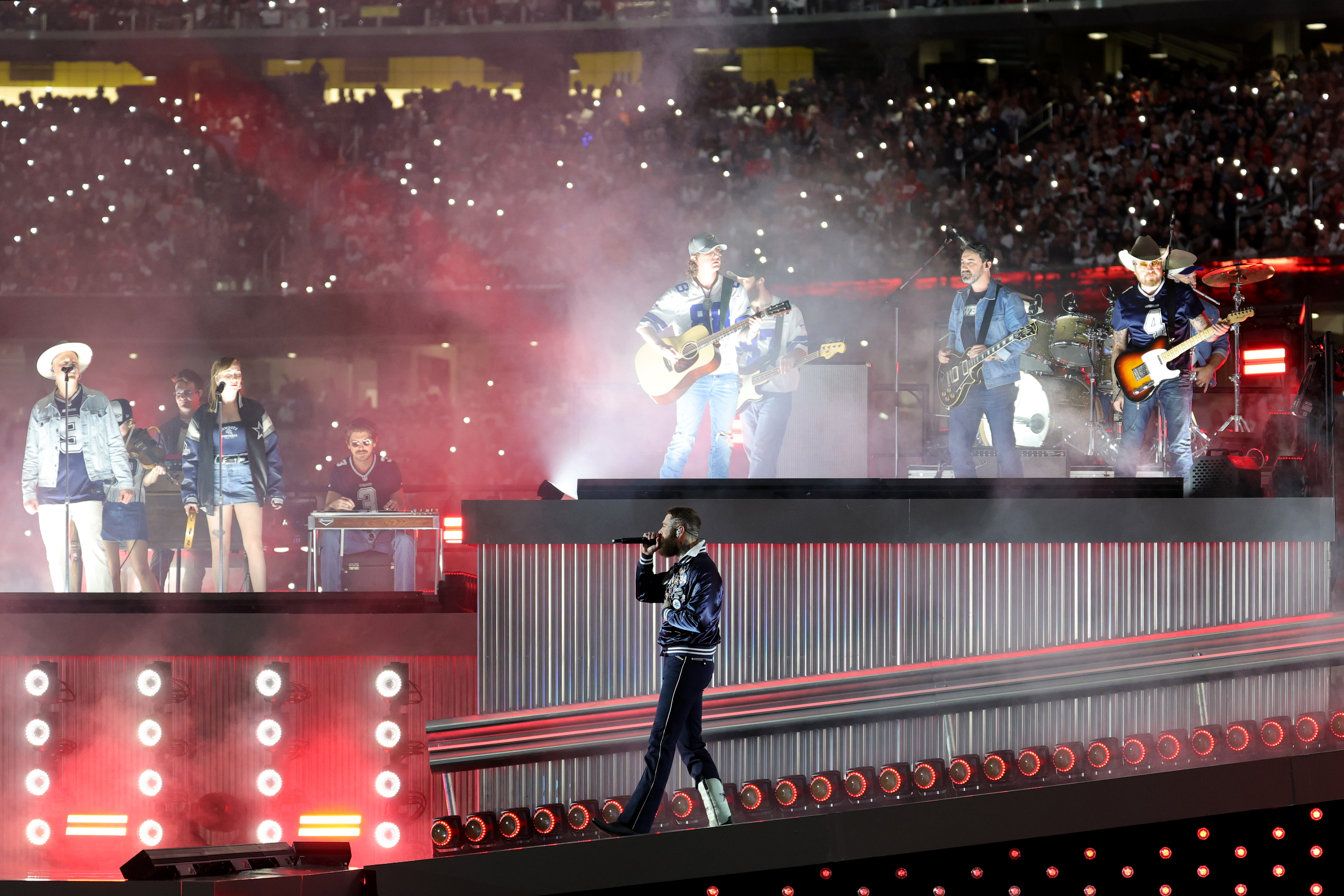 Post Malone performs with a full band and background vocalists as fans light up the stadium during halftime of the Cowboys vs. Chiefs game on November 27, 2025 | Source: Getty Images