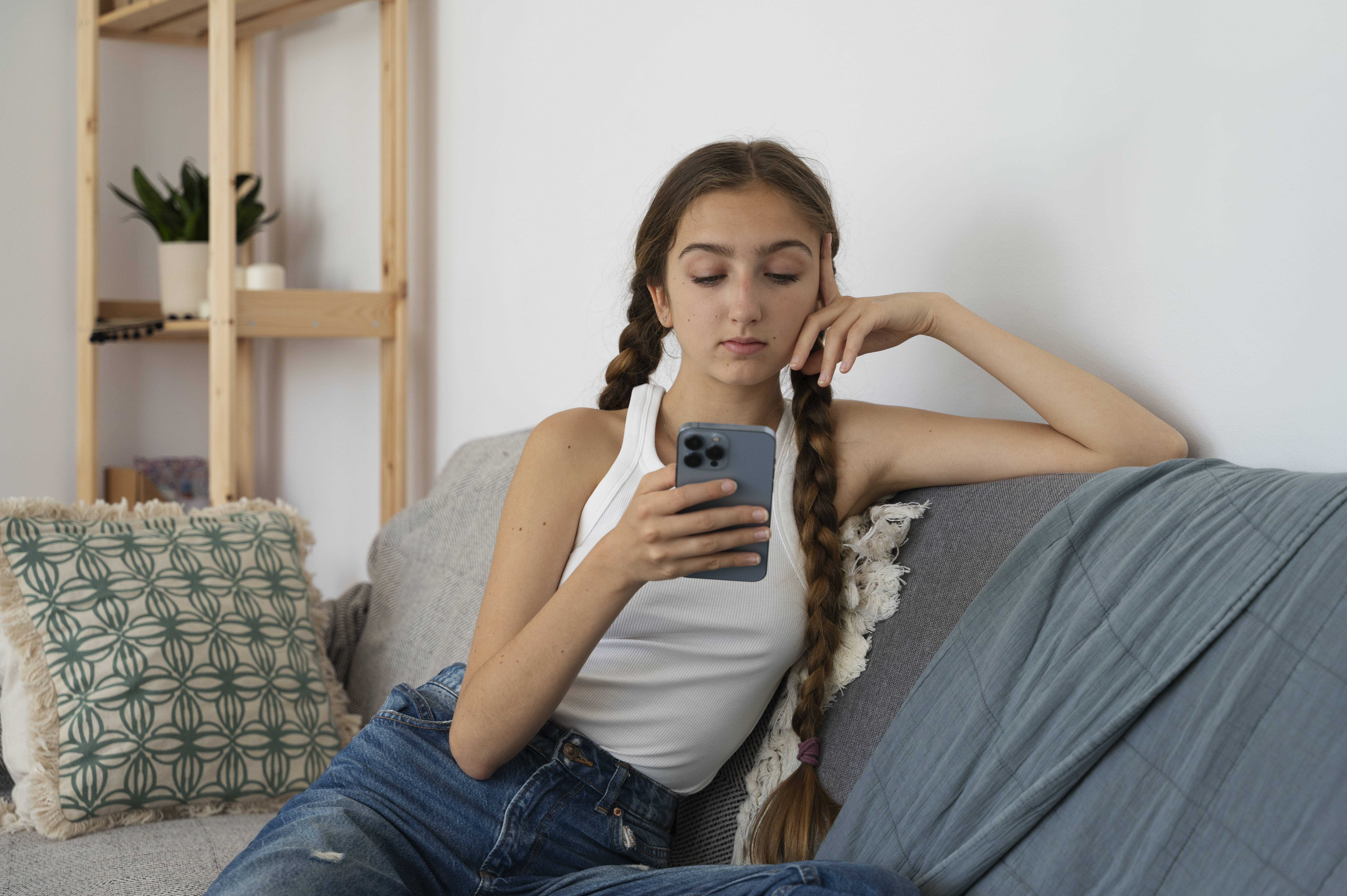 Young girl sitting on a couch and staring at her cellphone | Source: Freepik