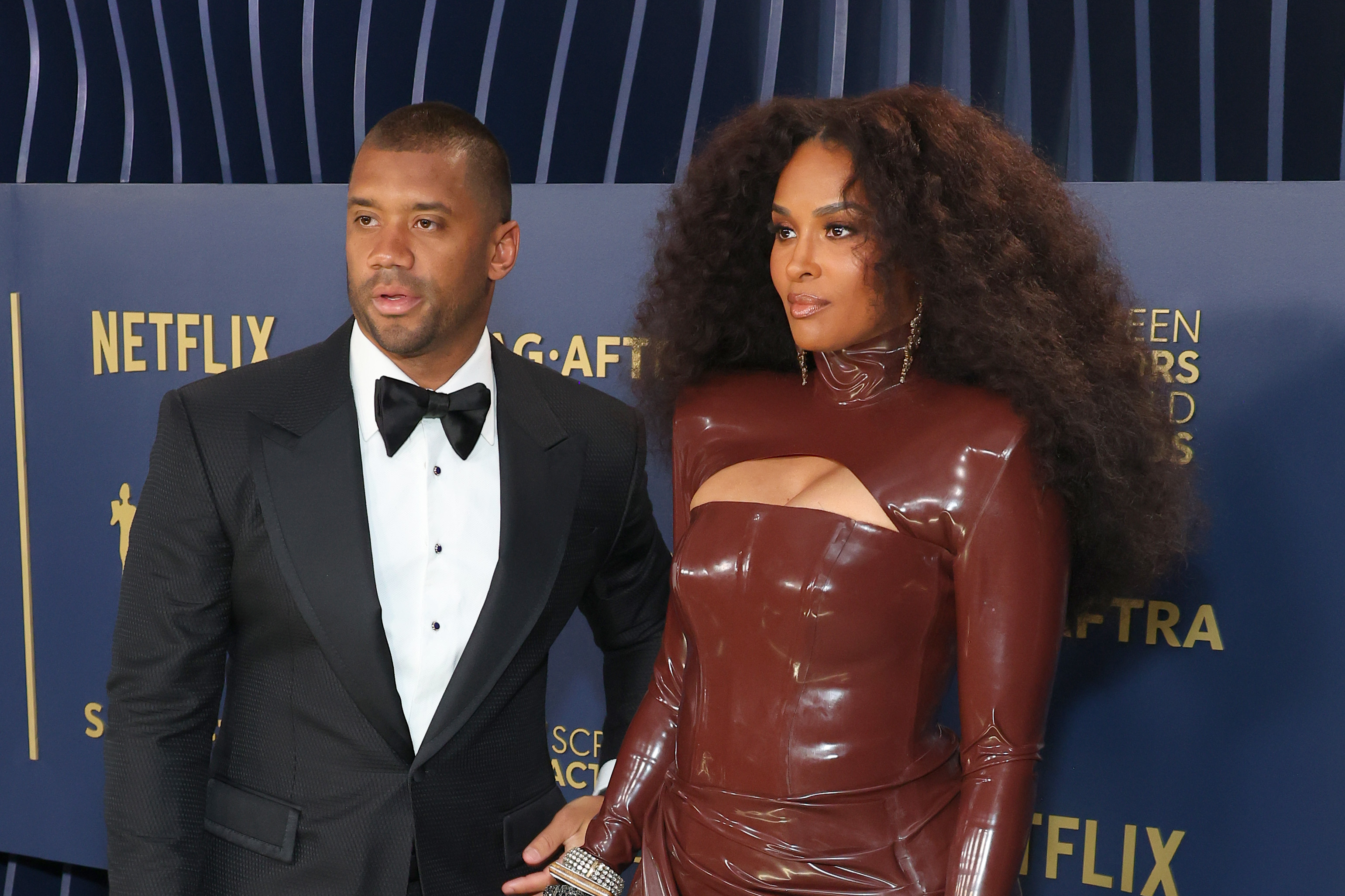 Russell Wilson and Ciara arrive at the 30th Annual Screen Actors Guild Awards, turning heads with a bold mix of classic tailoring and high-fashion drama. Her sculpted brown gown and his sharp tuxedo contrast strikingly against the dark backdrop as they stand poised side by side.