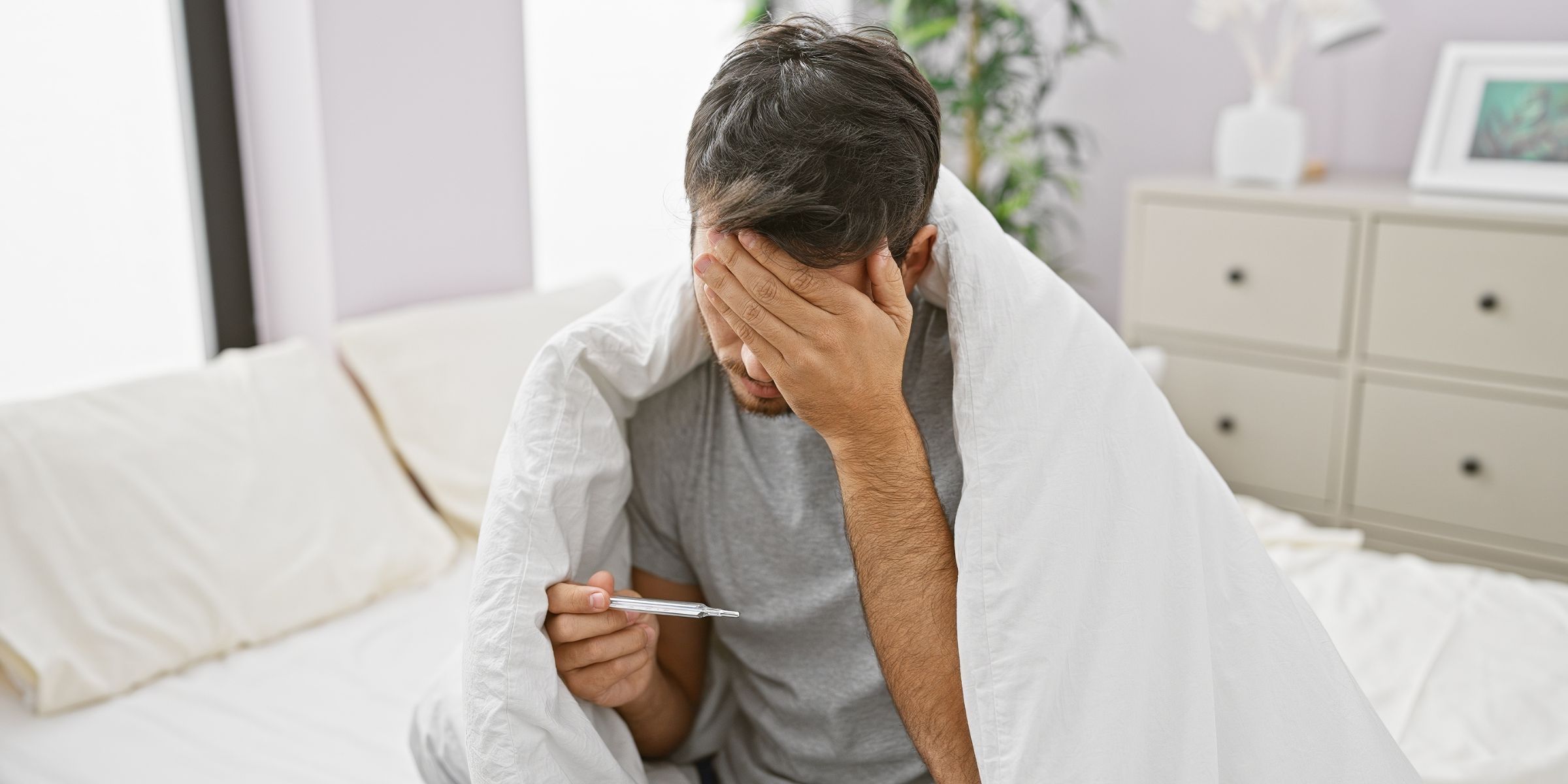 A man sitting in bed and checking his temperature | Source: Shutterstock
