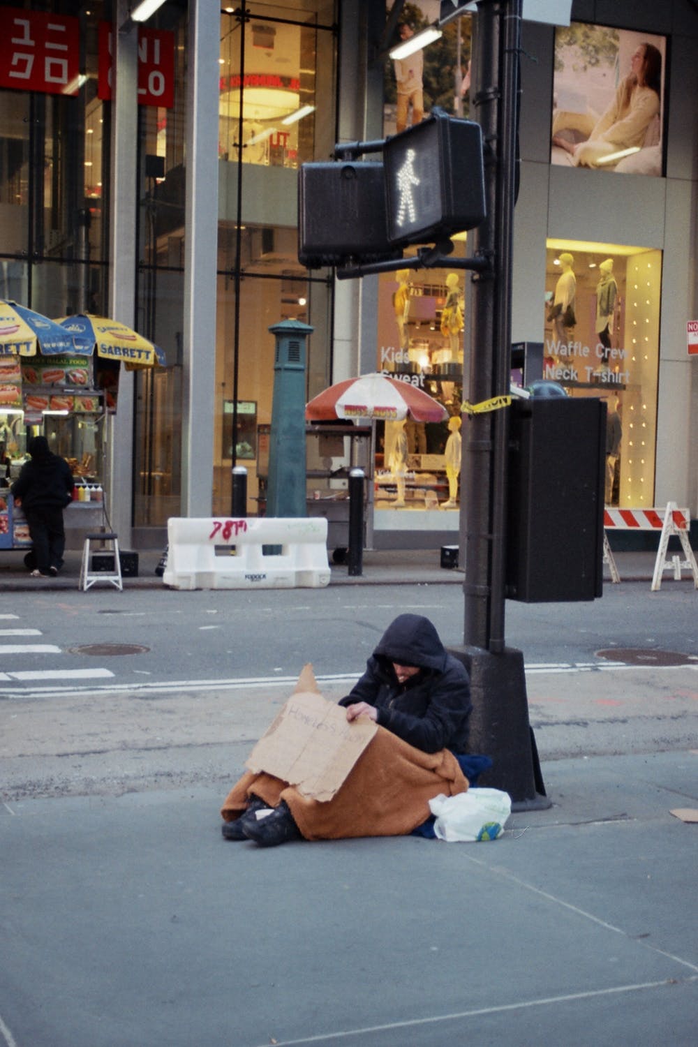 Un hombre sin hogar sentado en una acera, recostado de un poste. | Foto: Pexels