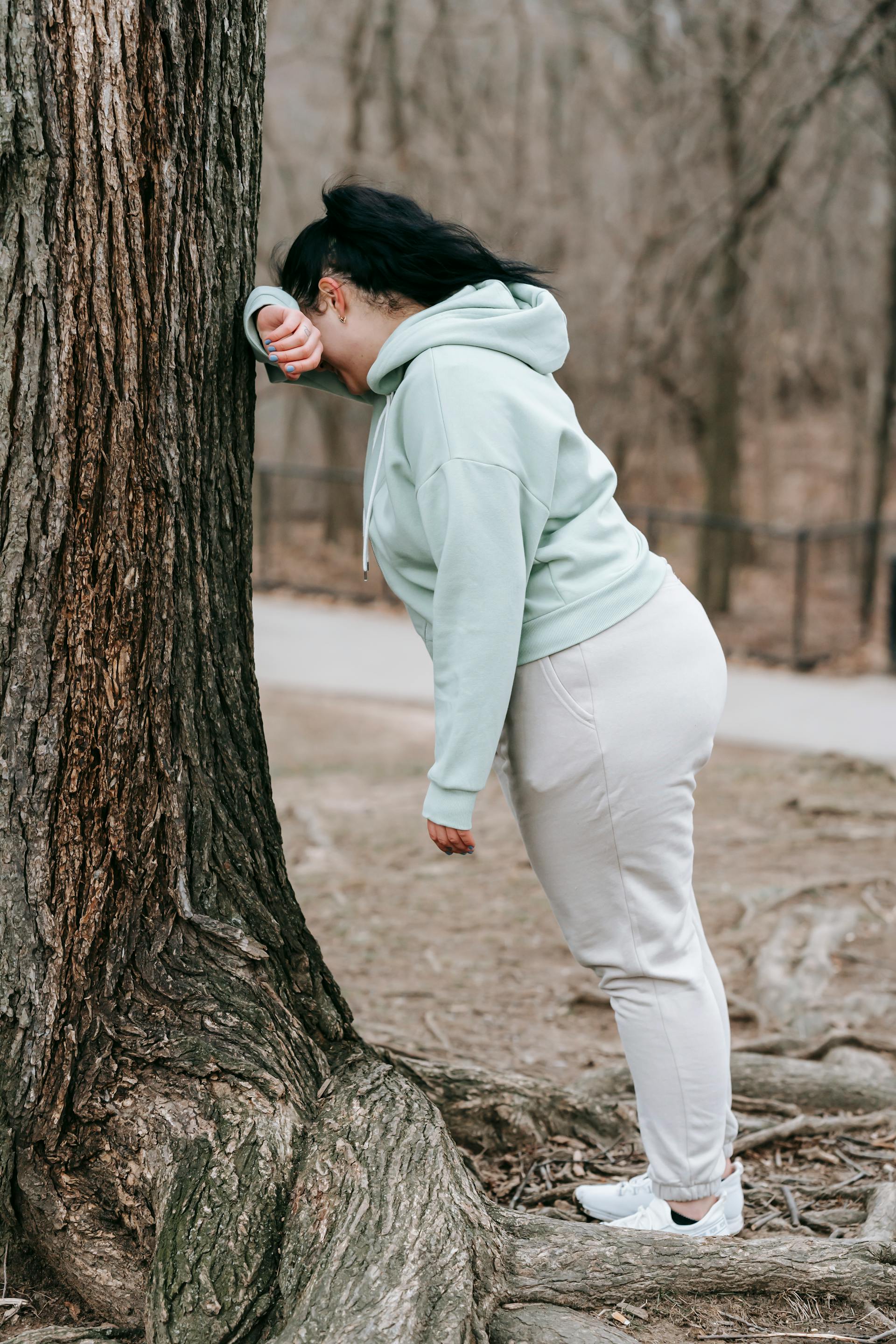 A woman in activewear leaning on a tree in a park | Source: Pexels
