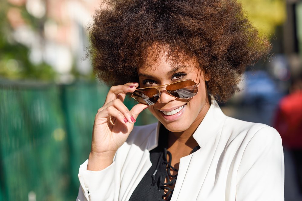 Mujer usando gafas de sol de tipo aviador y una chaqueta blanca con camiseta negra. | Foto: Shutterstock
